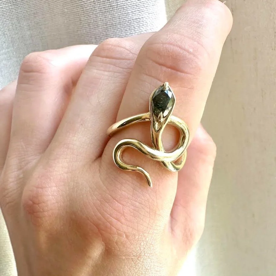 A gold snake-shaped ring with a dark gemstone on a person's finger.