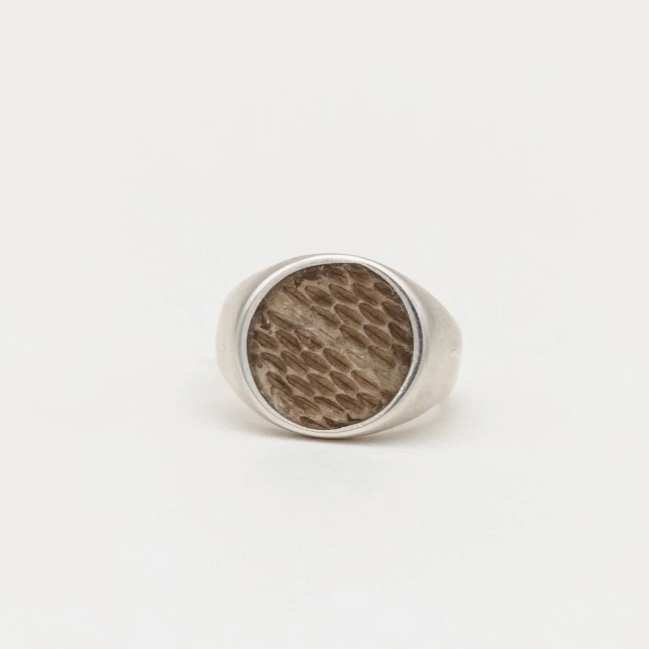 A ring with a round face featuring a textured light brown pattern, set in a silver band, on a white background.