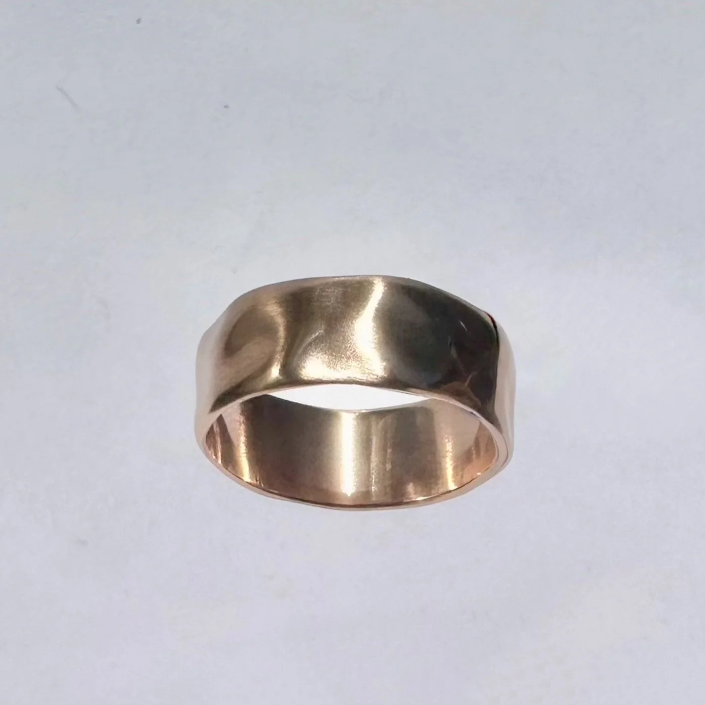 A wide, shiny metallic ring with a hammered texture, placed against a plain white background.