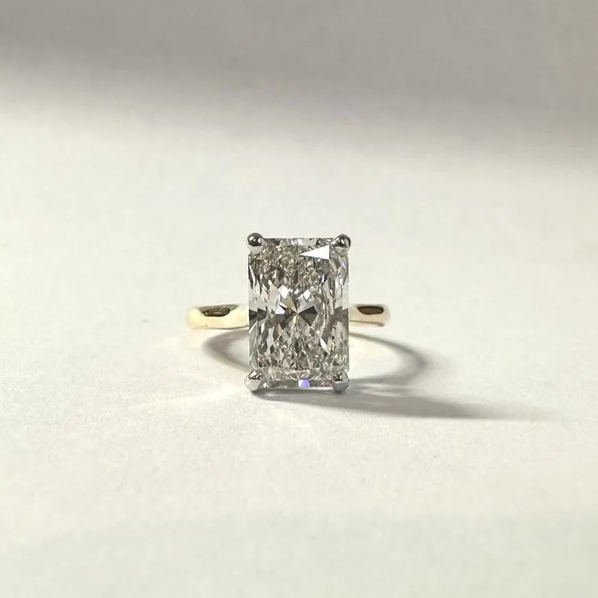 A solitaire engagement ring with a large rectangular cut diamond set in a simple band on a plain, light background.