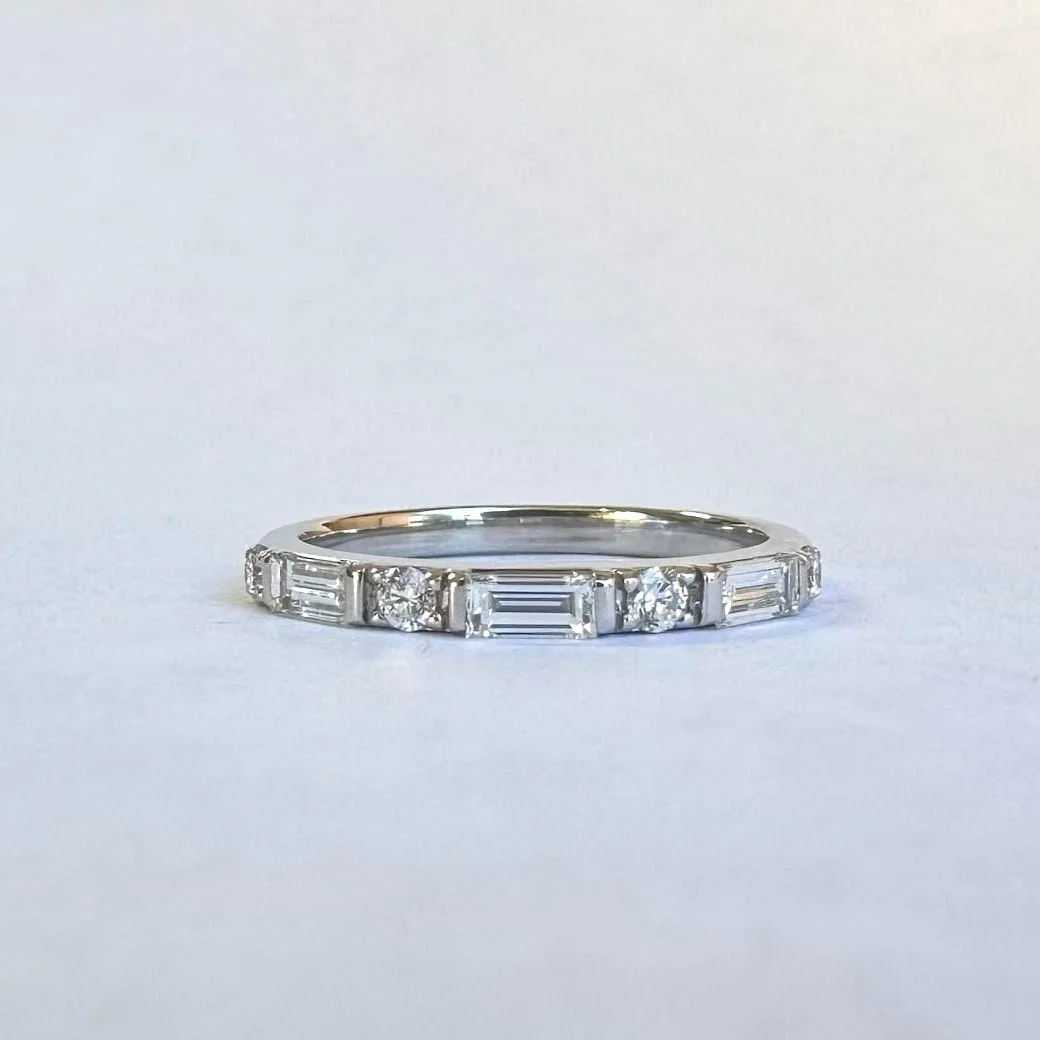 A silver ring with alternating round and rectangular cut diamonds set in a thin band against a plain light background.