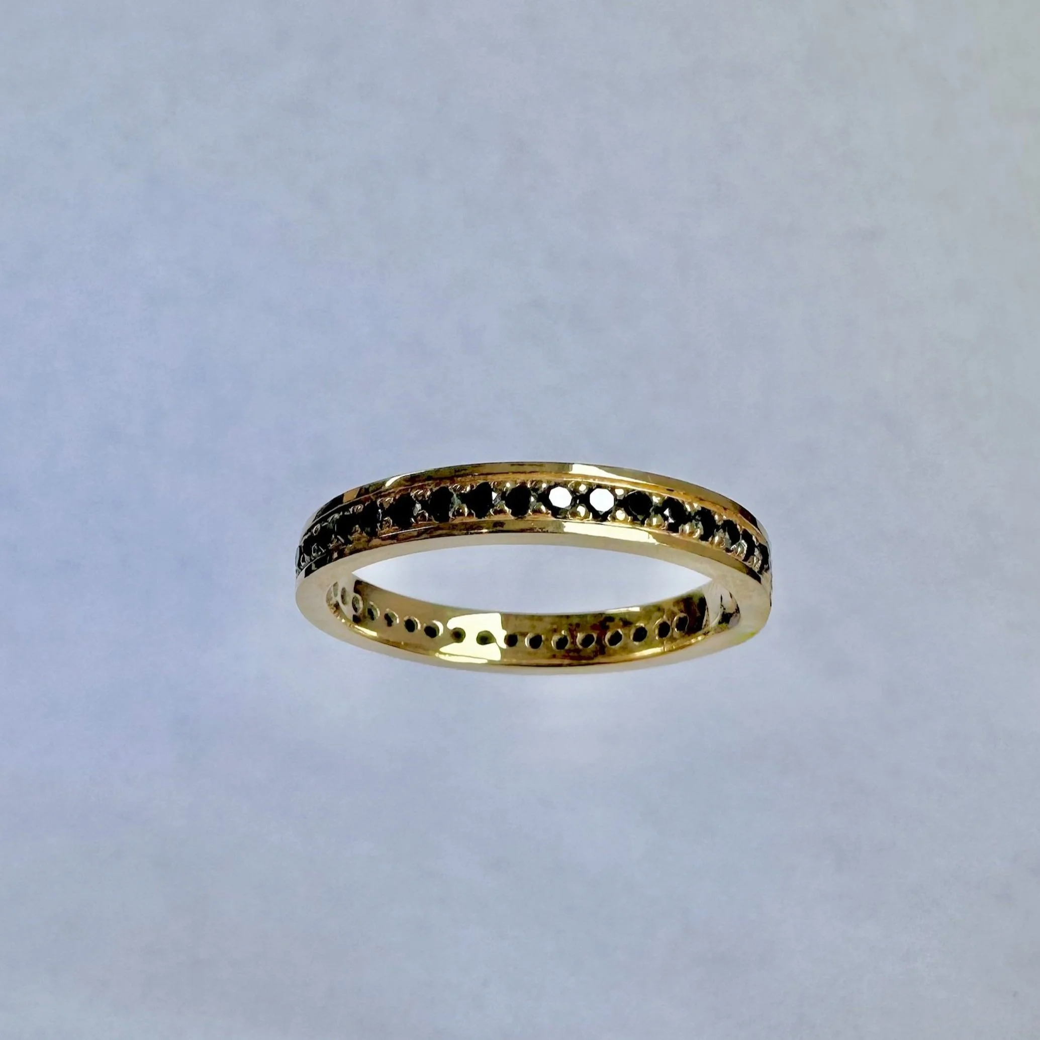 Gold ring with black gemstones on a light gradient background.