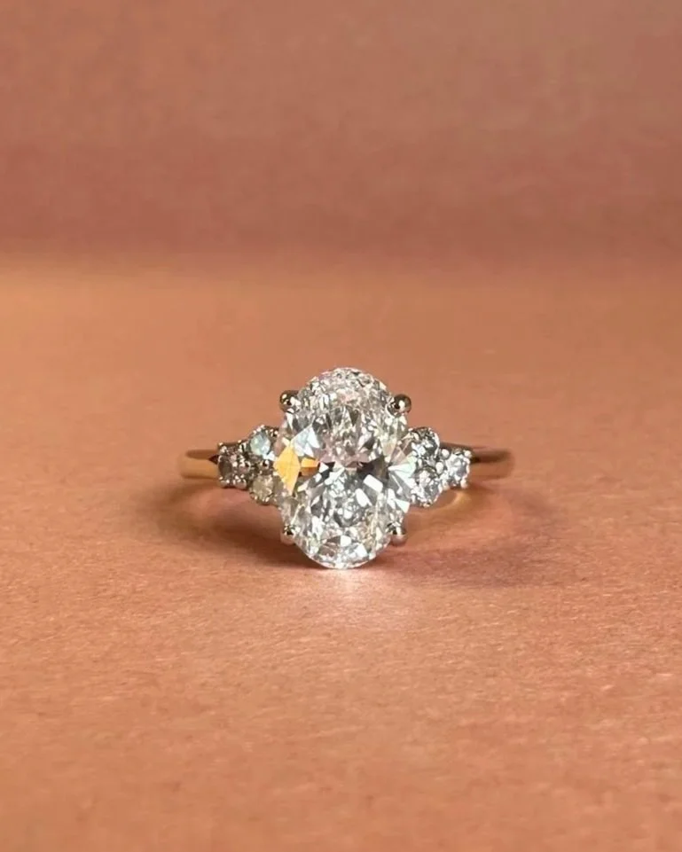 A diamond ring with a large central diamond and smaller surrounding diamonds on a pinkish surface.