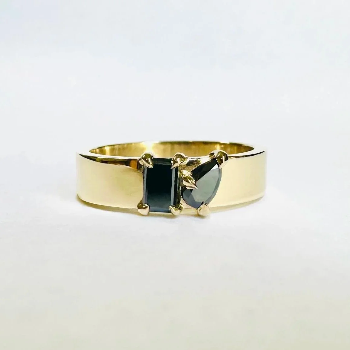 Gold ring with three dark gemstones set in a row against a white background.