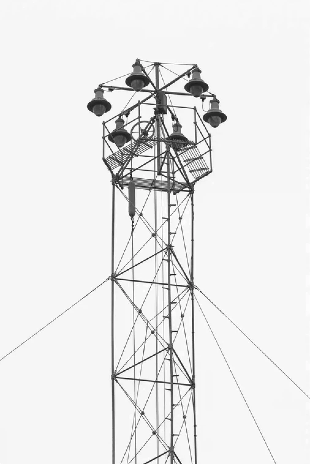 Black and white photo of a tall metal radio or communication tower with multiple antennas and lights on a plain sky background.