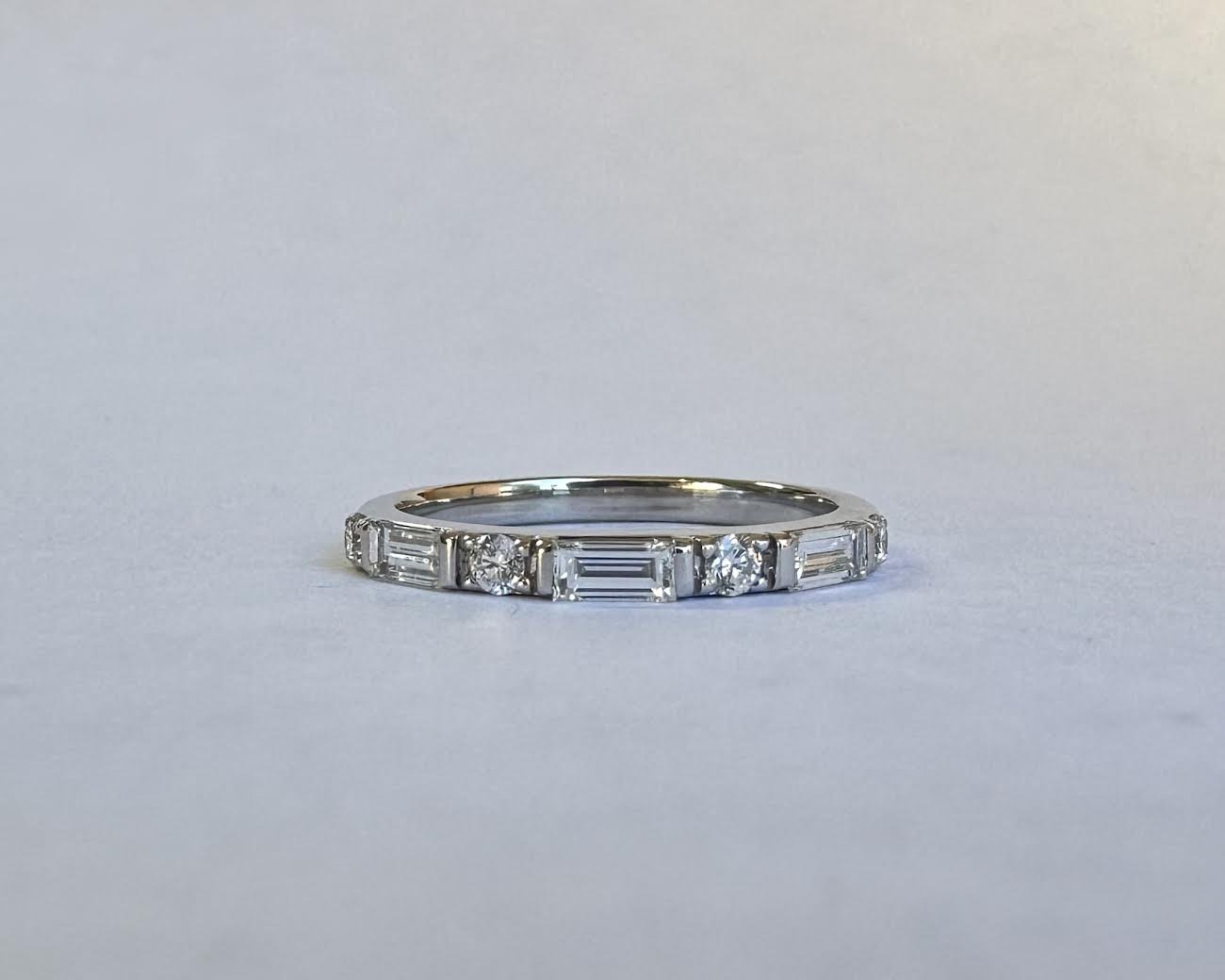 A silver ring with alternating square-cut and round diamonds set along the band.