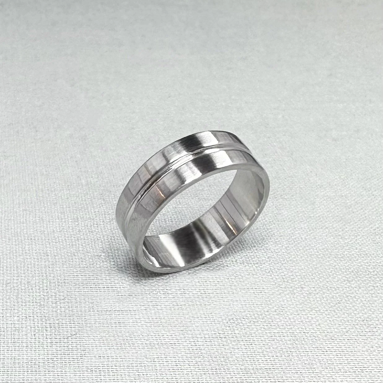 A silver ring with a centered groove, resting on a textured light-colored surface.