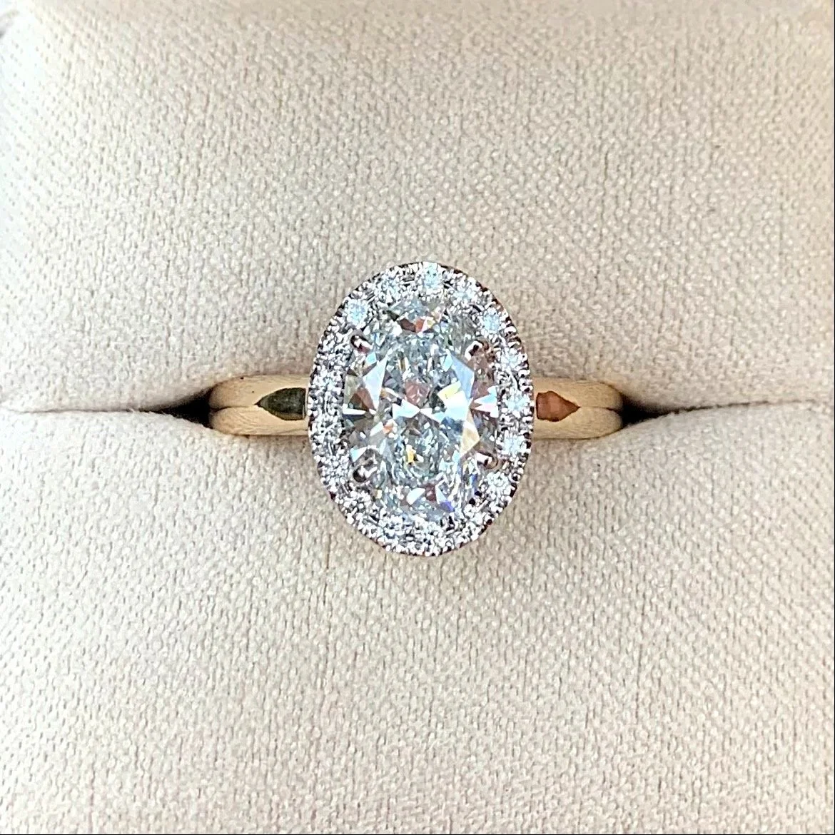 Oval diamond ring with a halo of smaller diamonds on a gold band.