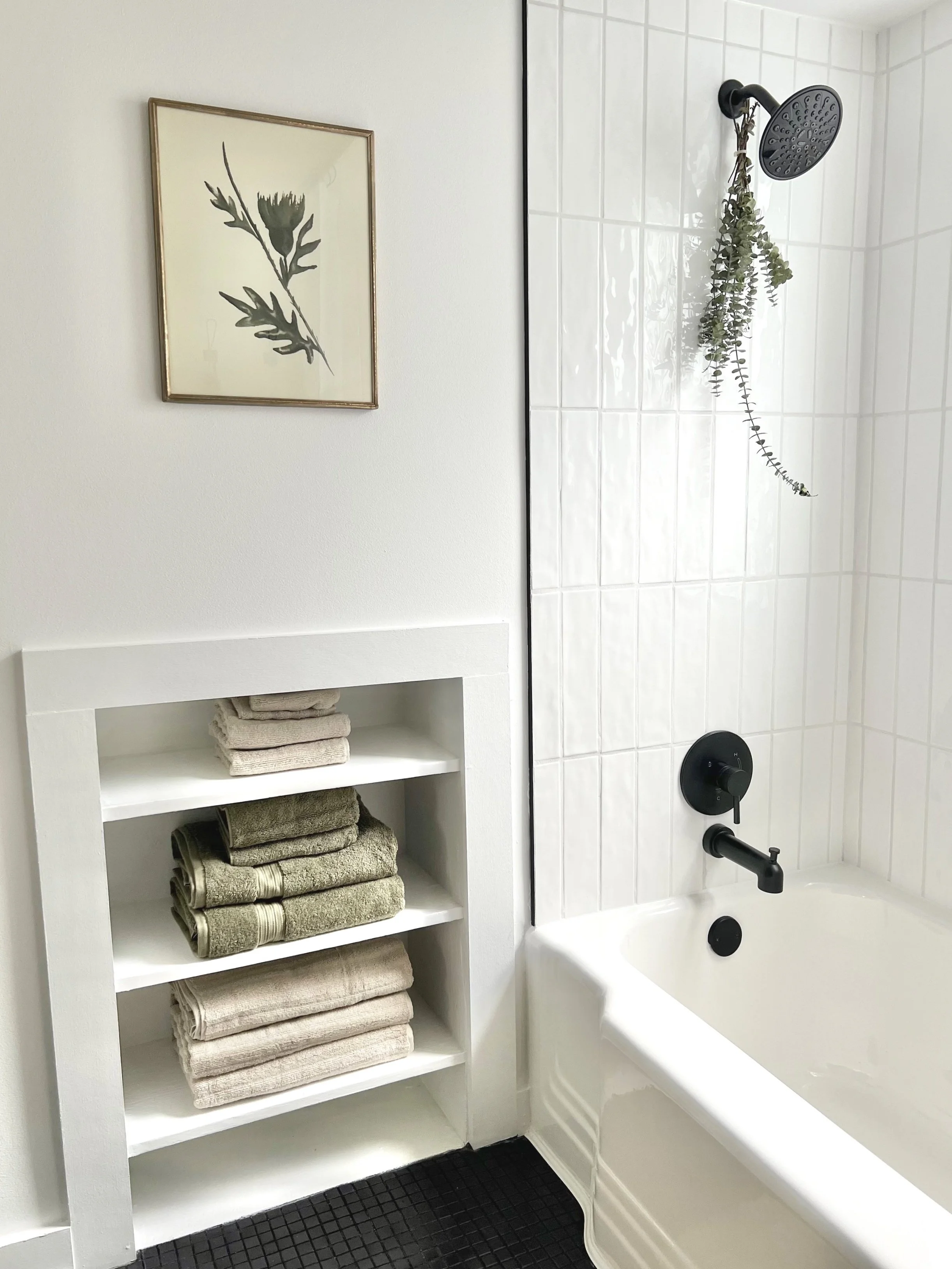 Restored bathroom with white horizontal tile, black accents, and home decor including towels and a picture of a leaf.