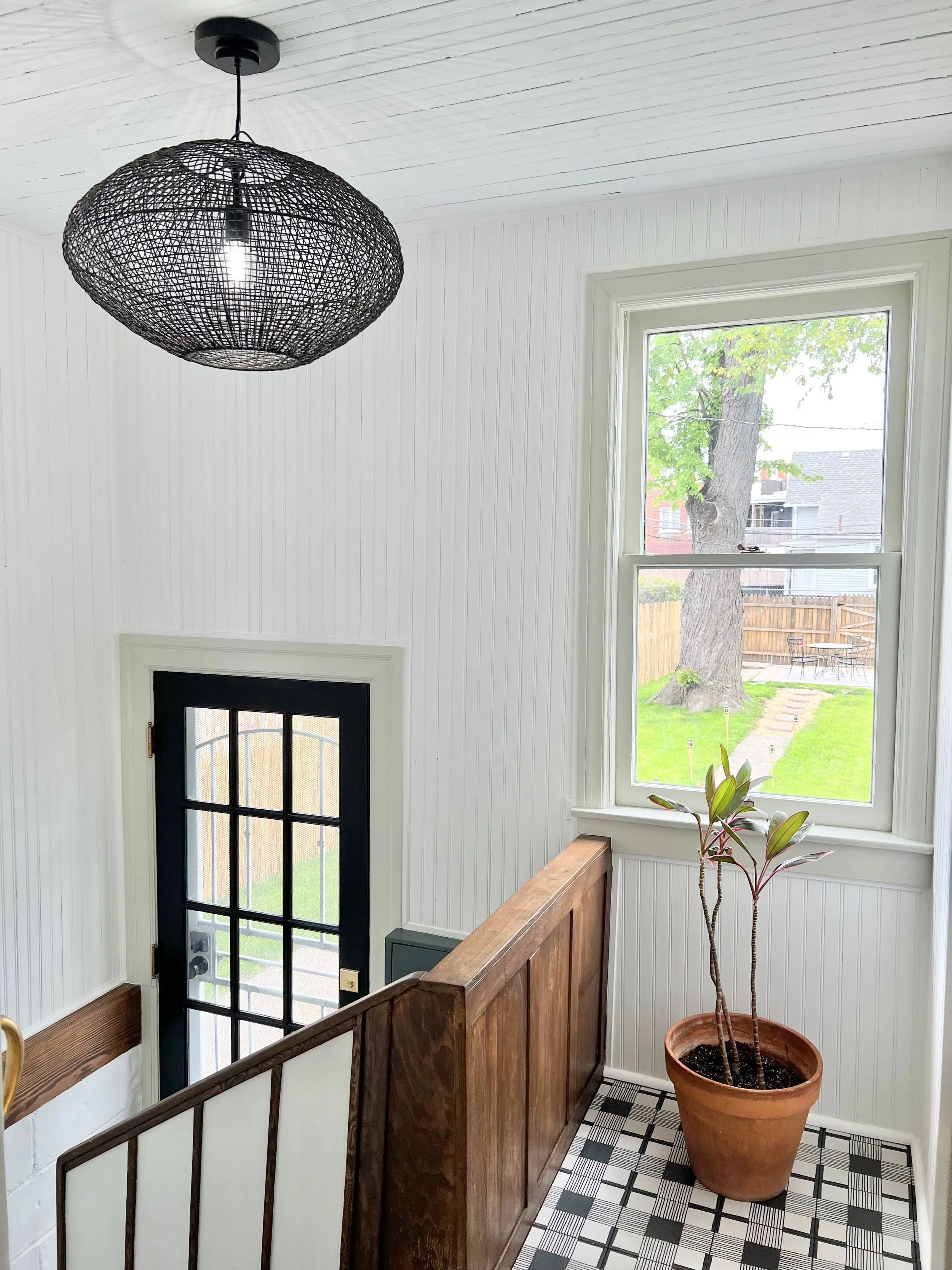 Back entrance with white clapboard, yarn pattern light fixture, restored wood banister and plant on new tile.