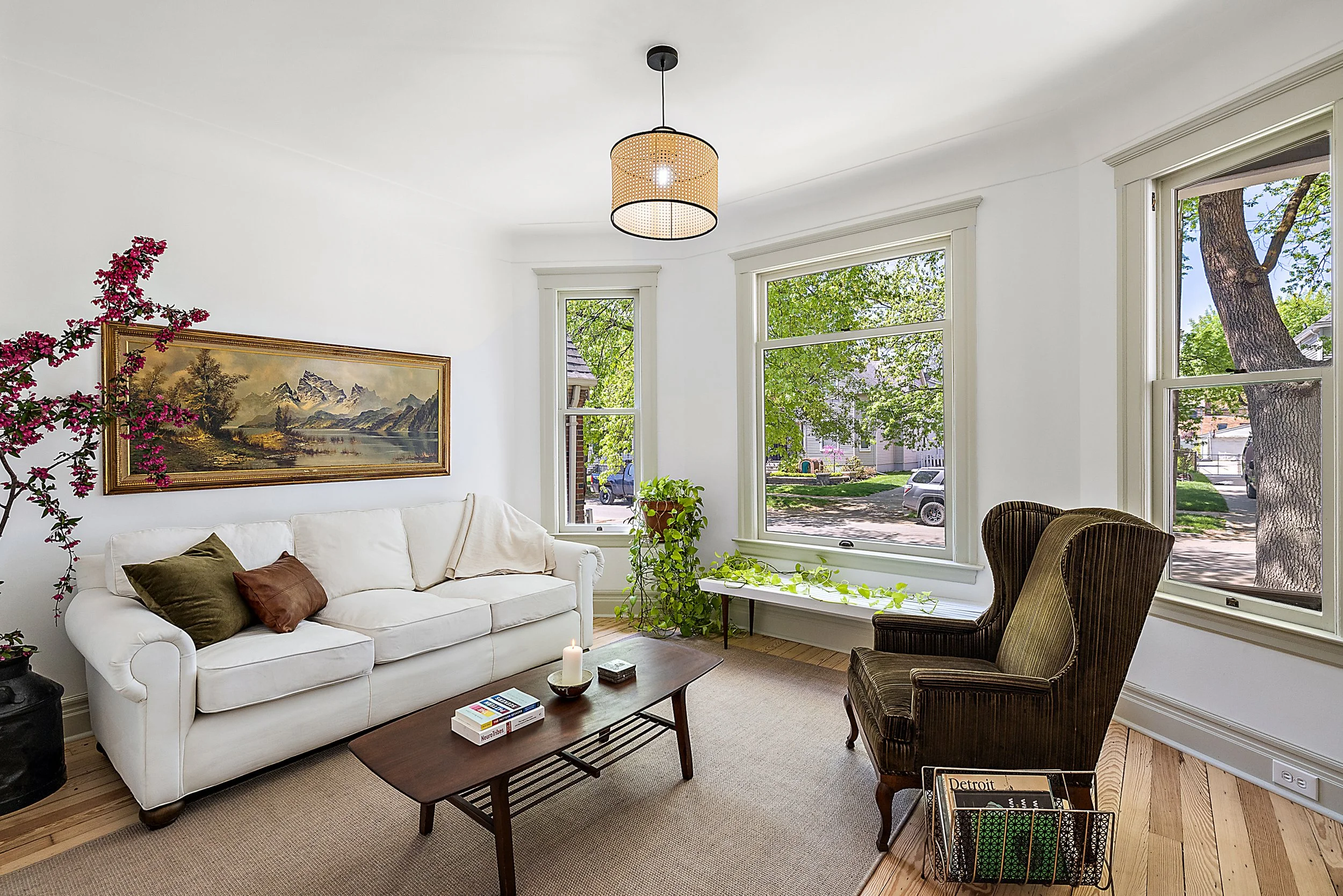 Restored living room with home decor, three front windows, white walls, green trim and a hanging pendant light. 