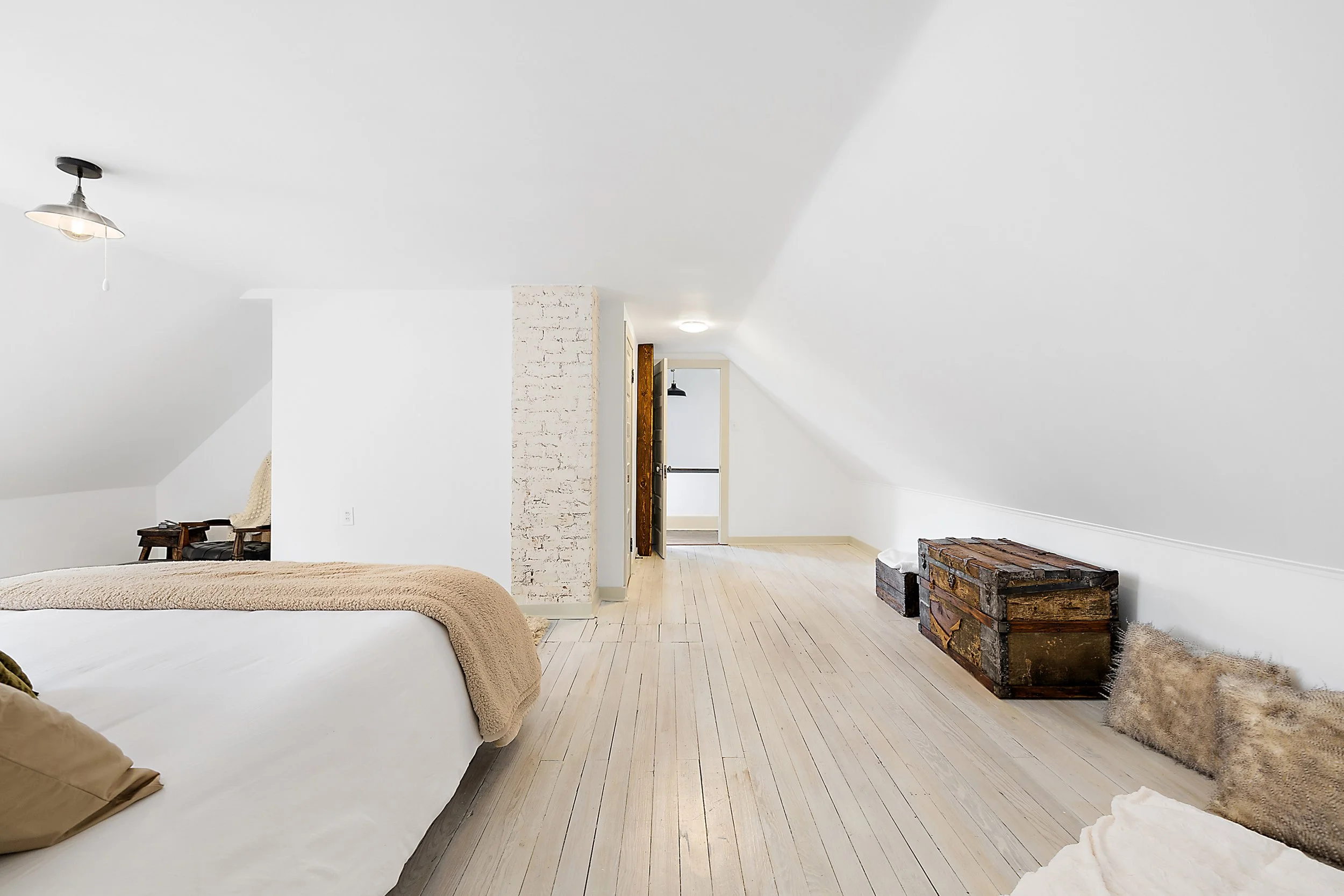 A renovated bedroom with renovated floors and walls. There is a hallway, a chimney and white walls. 