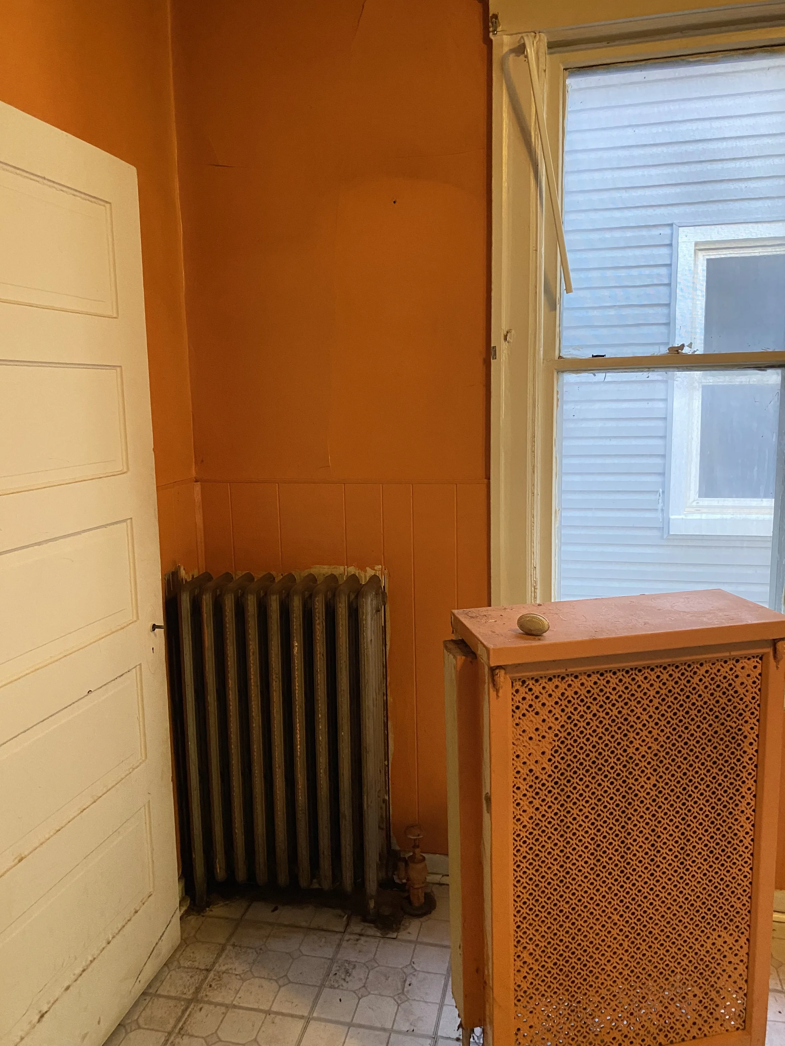 Damaged kitchen with orange walls and an old radiator. 