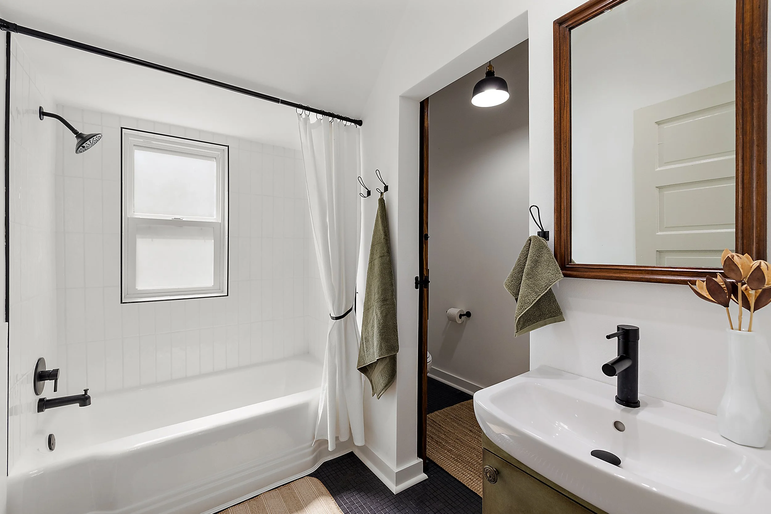 Renovated bathroom with a tub, black hardware, a sink, mirror, and doorway to the powder room. 