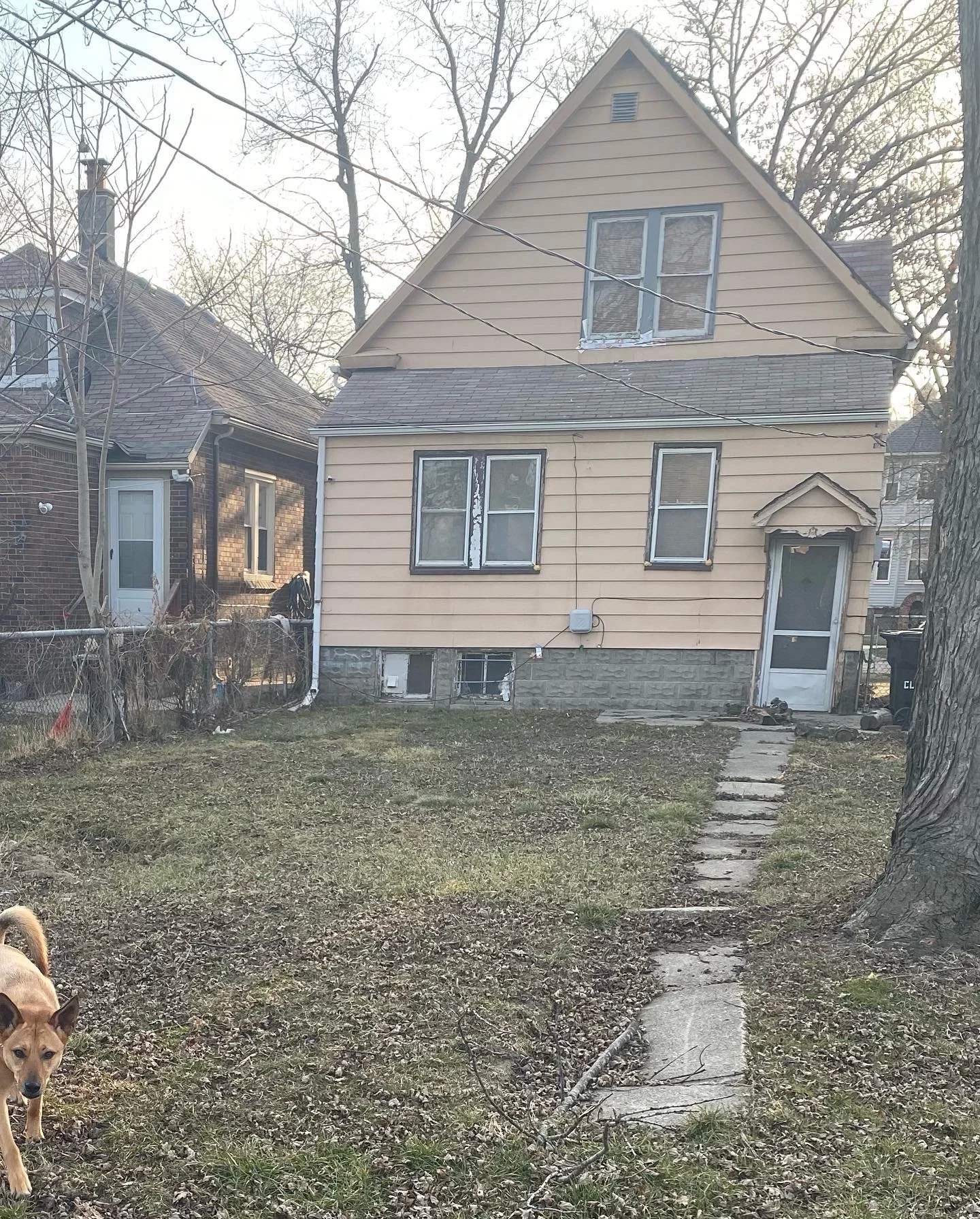 The back of a 1915 Edwardian house with a broken sidewalk. The house is painted a cream color. 