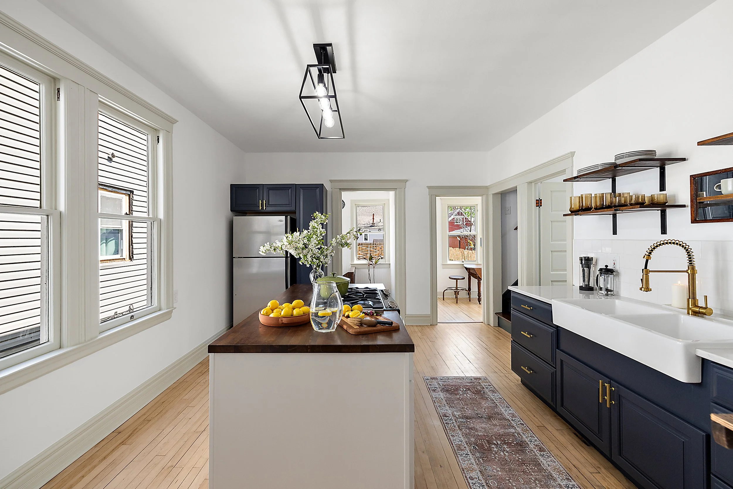 Renovated kitchen with green trim, maple floors, island with a butcher block counter top, blue cabinet, black light, and farm house style sink.