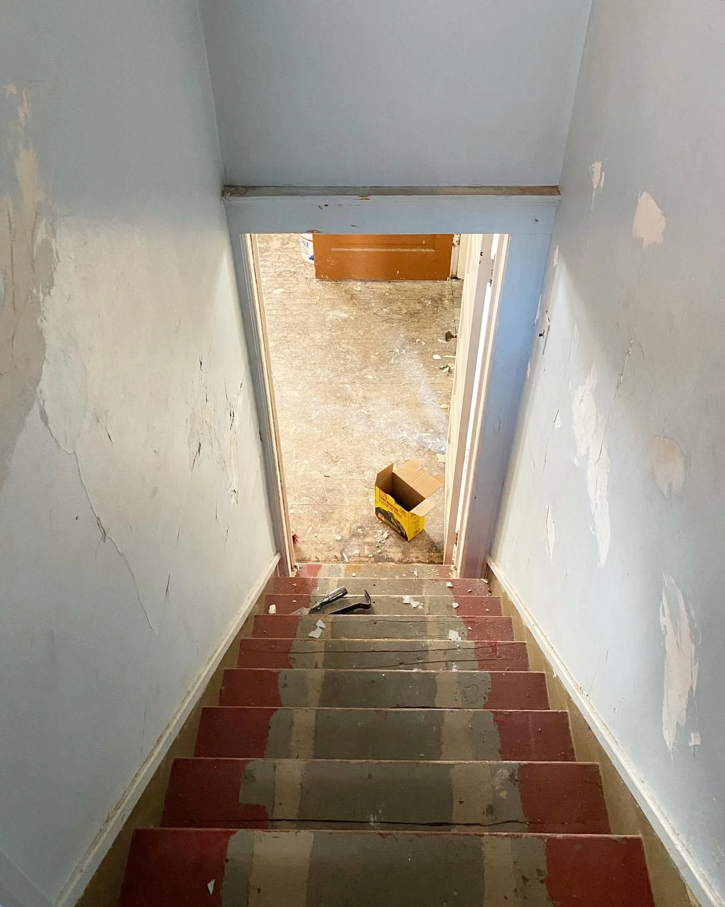 Stairwell before it's renovated with damaged blue walls and red broken stairs. 