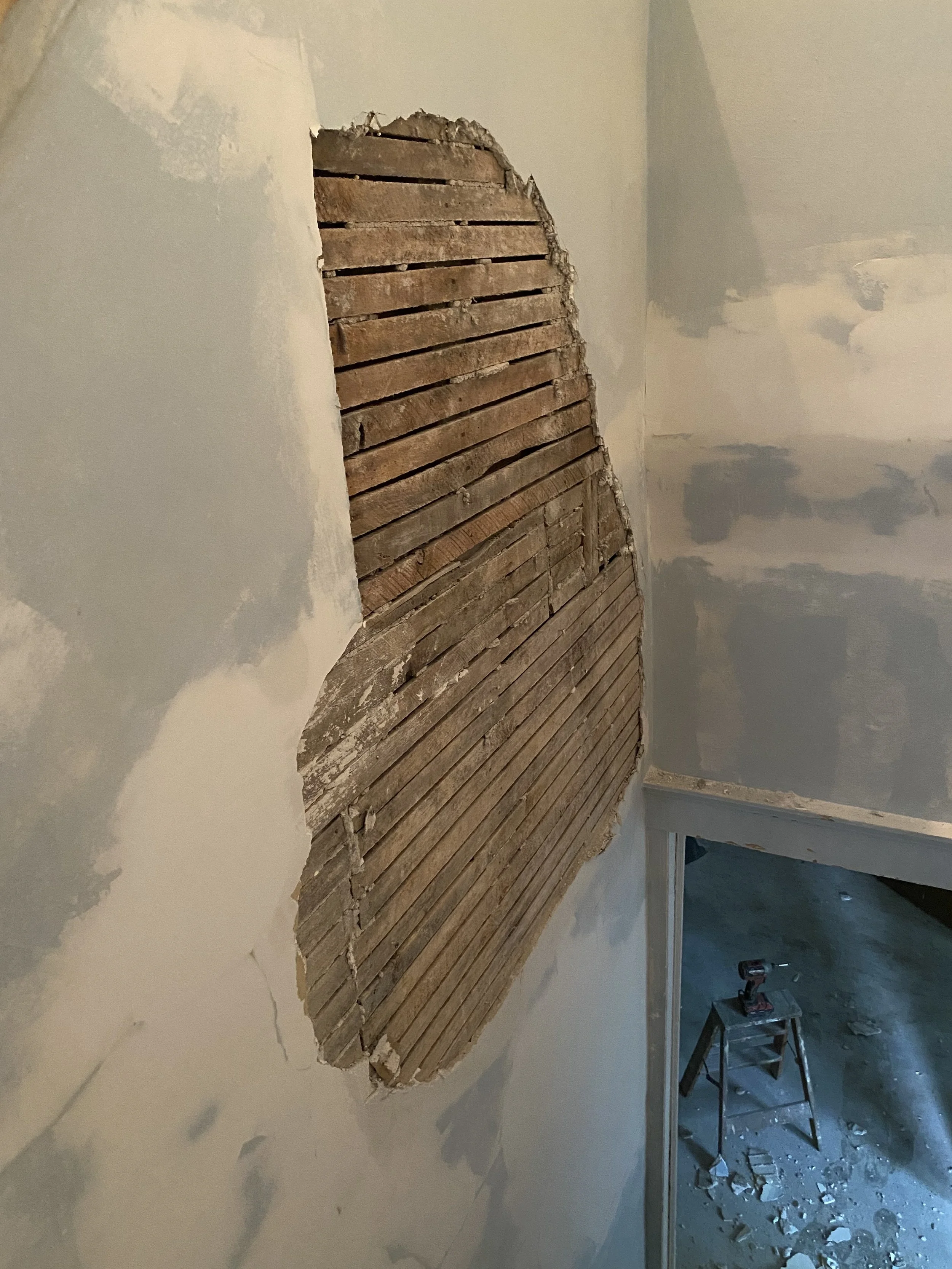 Damaged plaster wall in stairwell, showing lath. 
