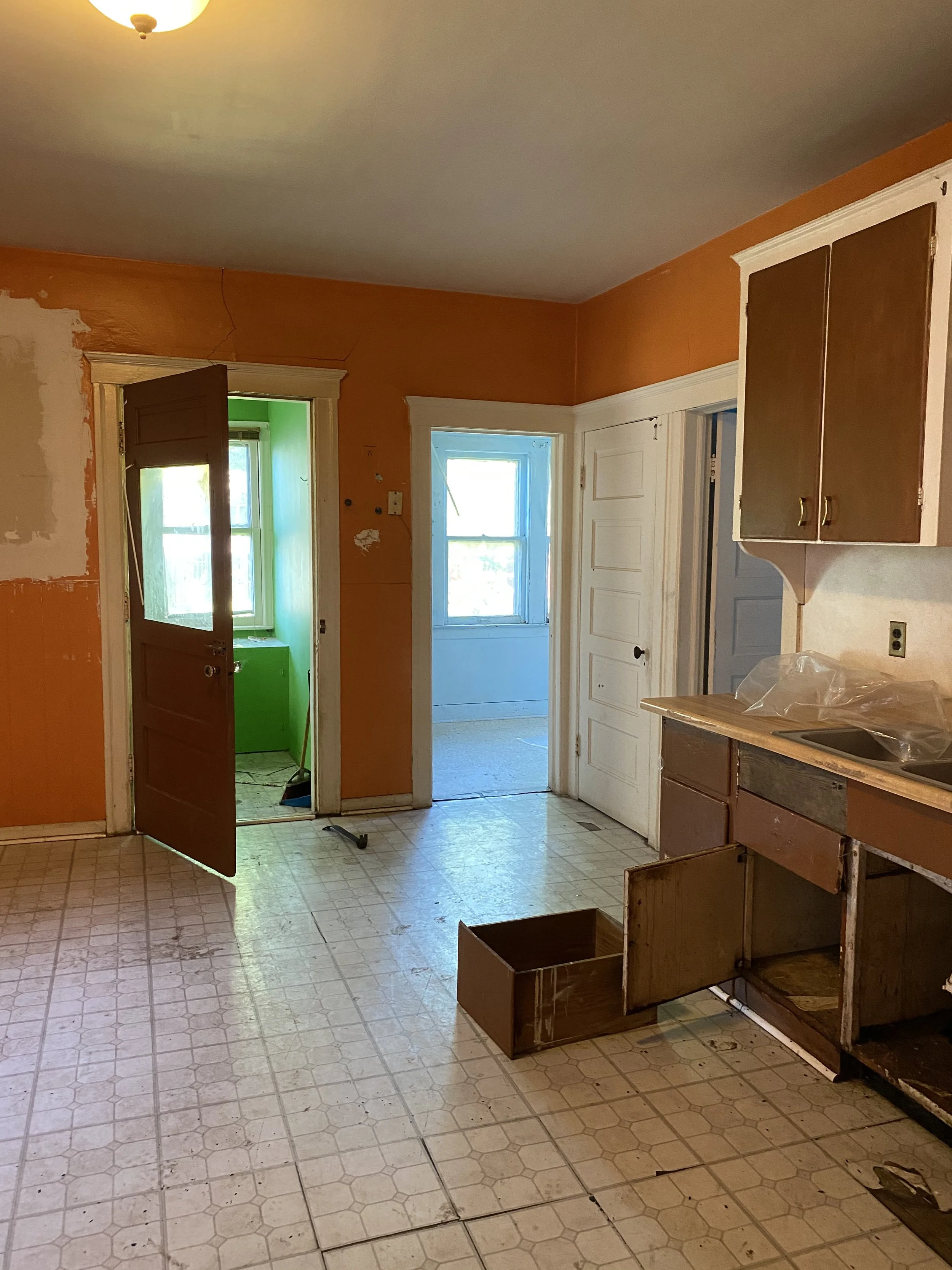 1915 kitchen before it's renovated with damaged walls, vinyl floors, and brown cabinets. 