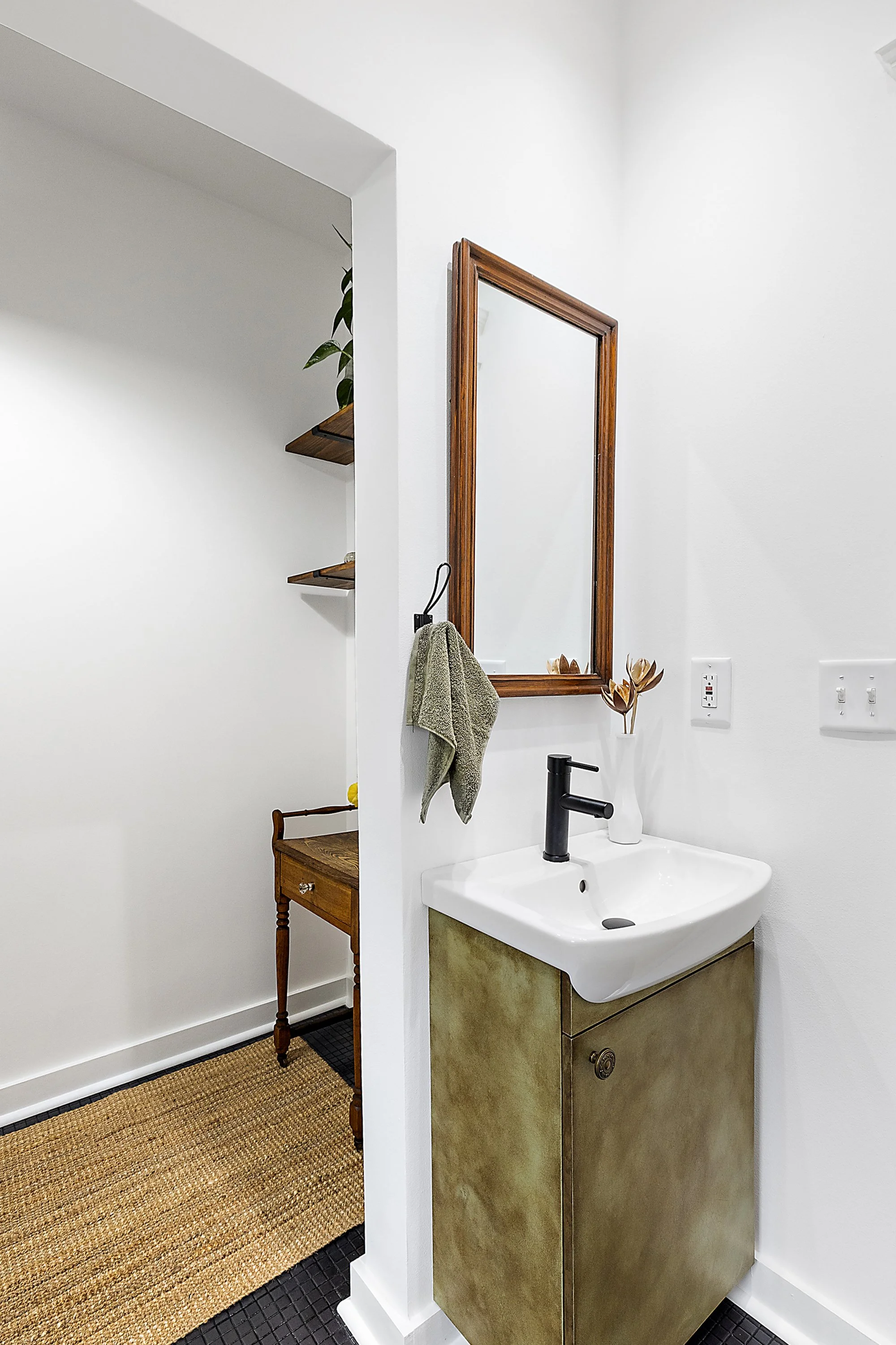Renovated bathroom with custom green cabinet, porcelain sink, black faucet, and wood mirror hanging on the wall. 