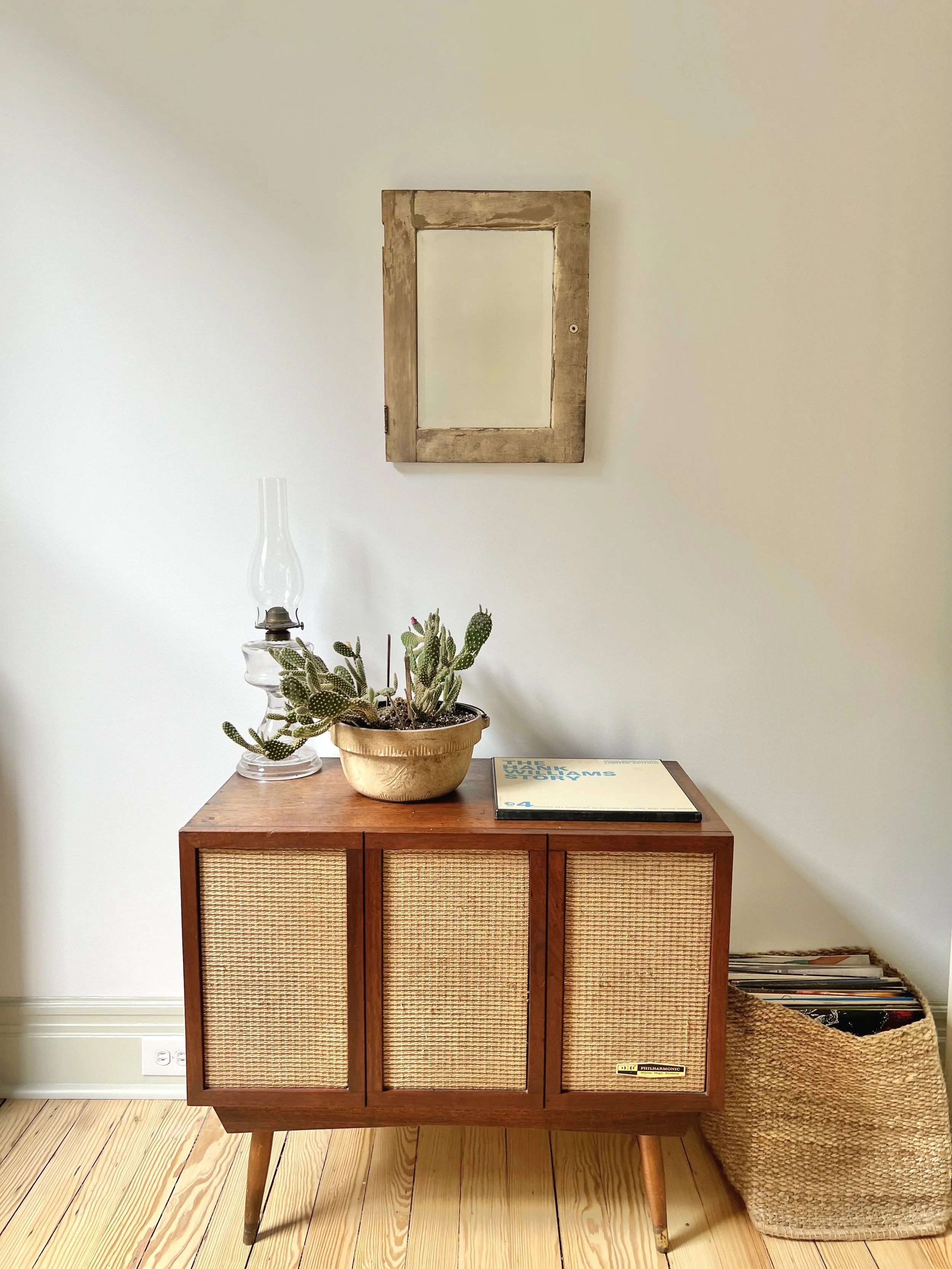 Vintage record stand on restored pine floors, with home decor, records, and mirror on painted wall.