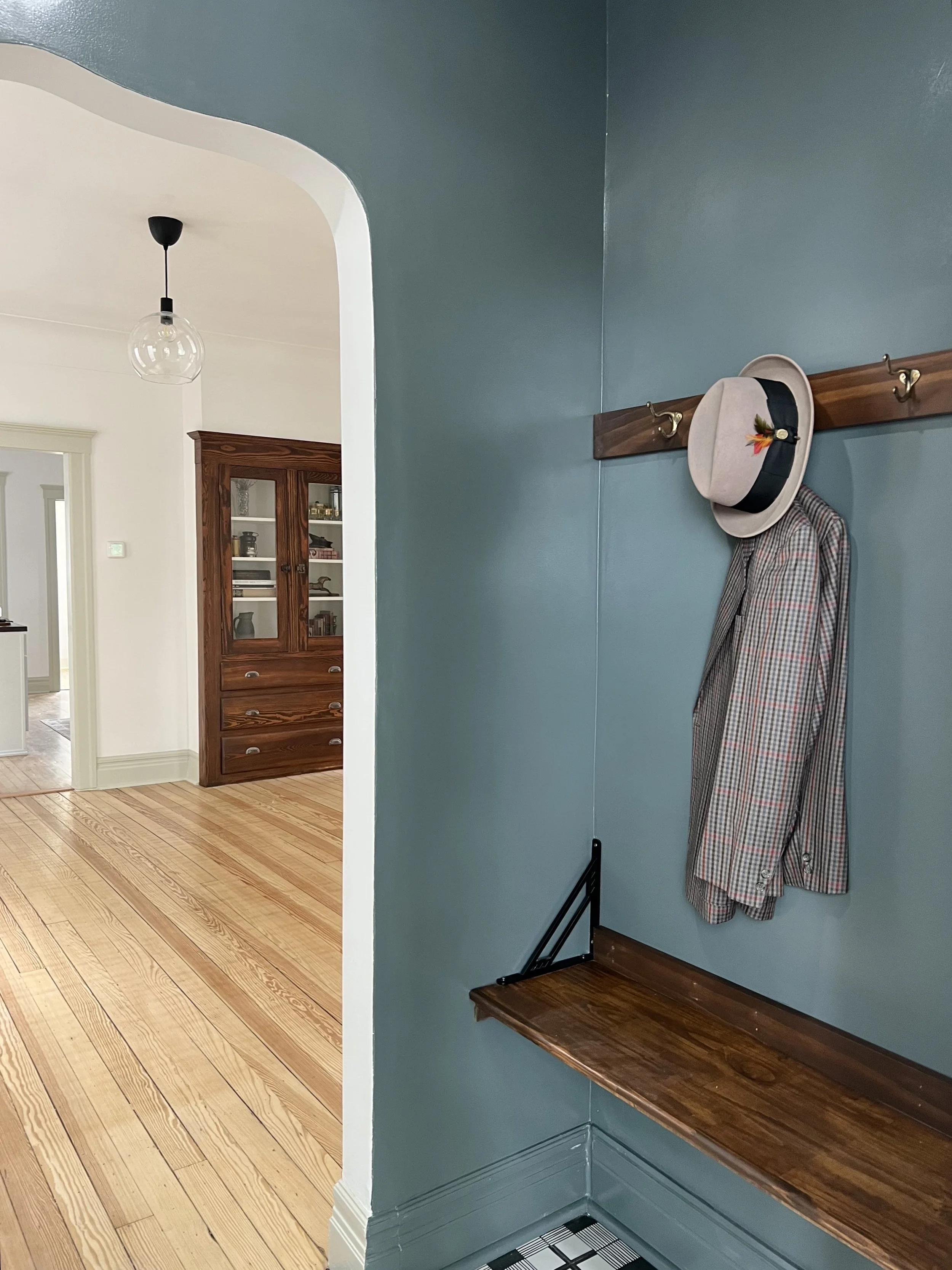 Restored 1915 entry way with seating, fresh paint, restored plaster walls and a hat and coat on a hook.