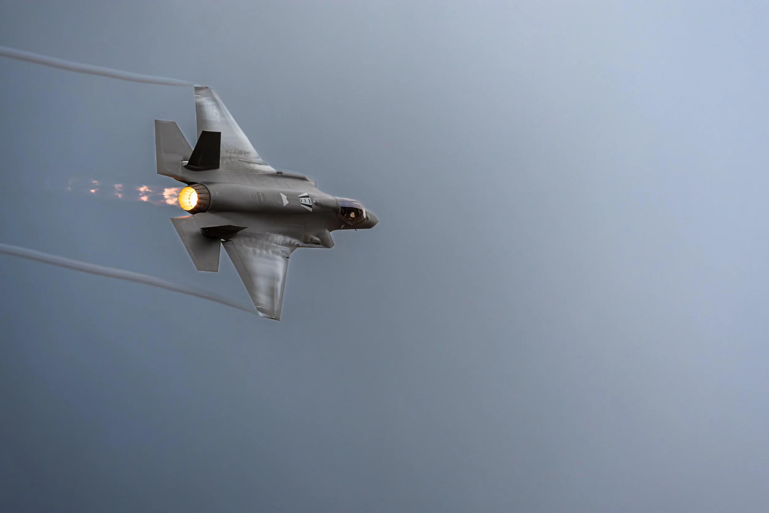 A fighter jet in mid-flight with afterburners on, flying through the sky and leaving contrails behind.