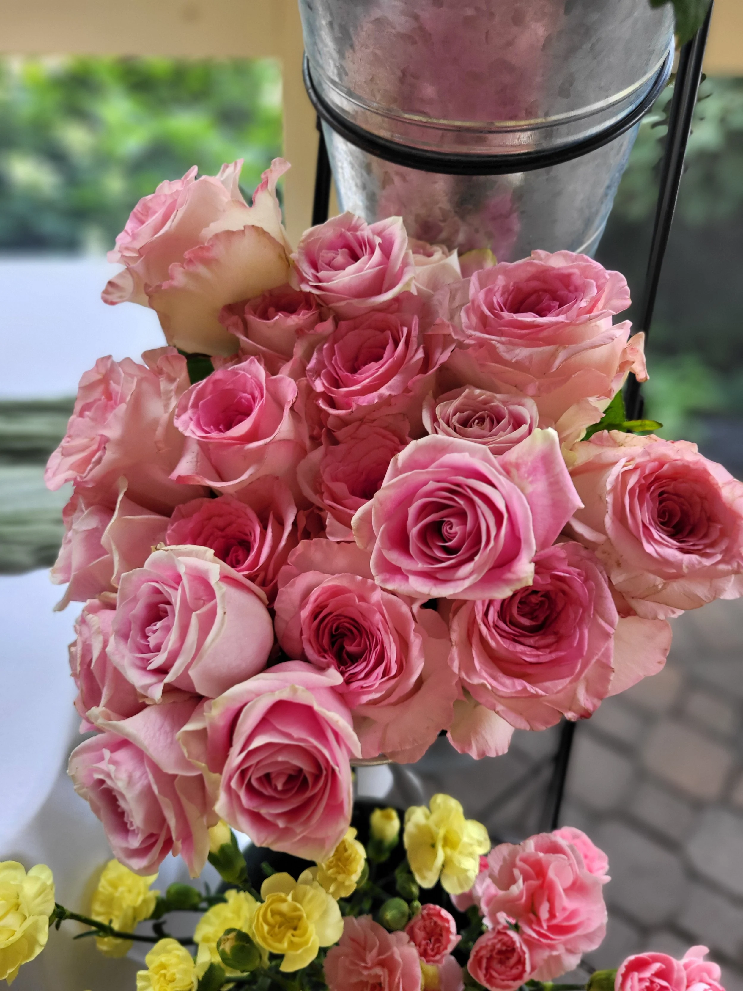 A bouquet of pink roses and yellow flowers arranged on a table indoors.