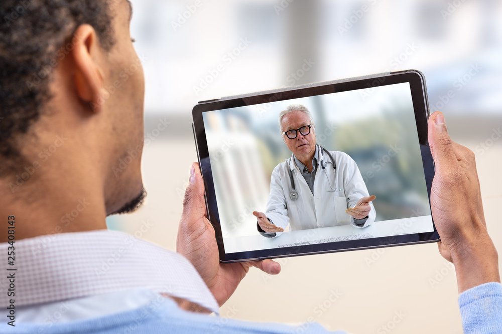 Person holding a tablet showing a video call with a doctor wearing glasses and a stethoscope.