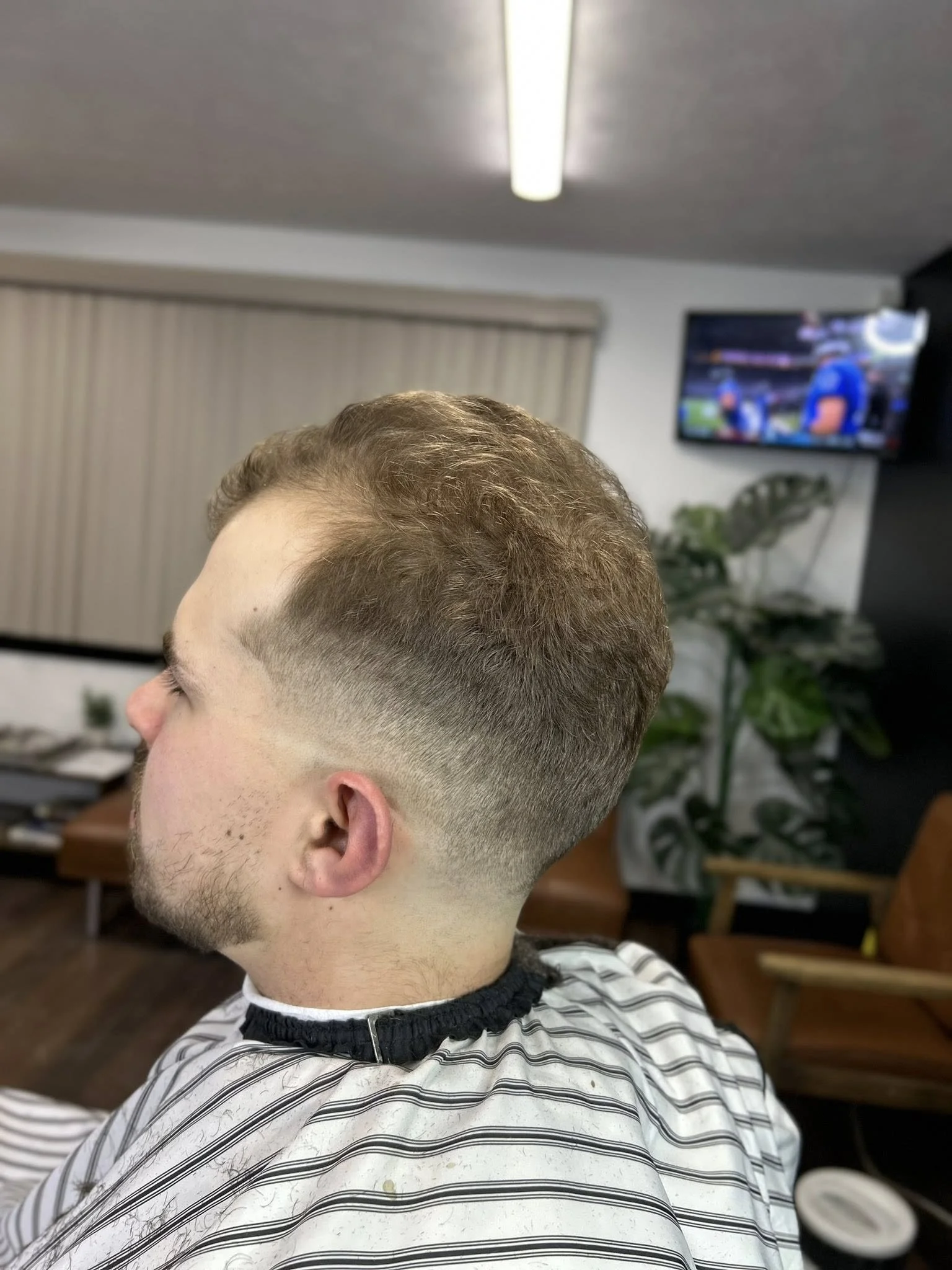 Young man with a fresh fade haircut sitting in a barbershop chair.