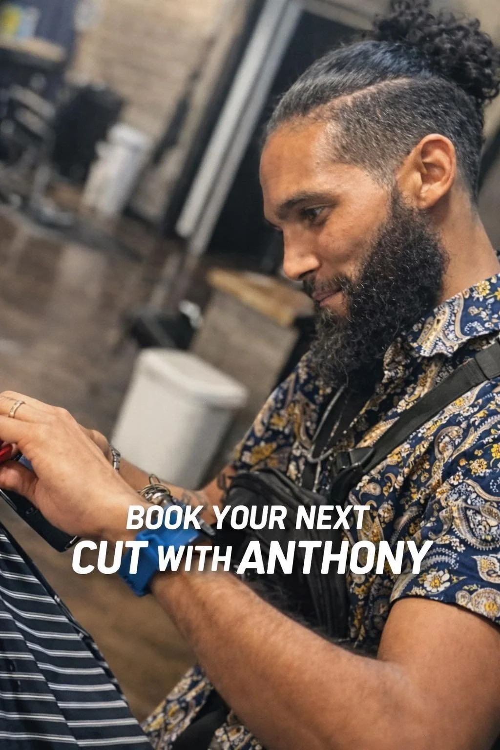 A man with a beard and curly hair receiving a haircut in a barbershop, with a text overlay promoting booking a haircut with Anthony.