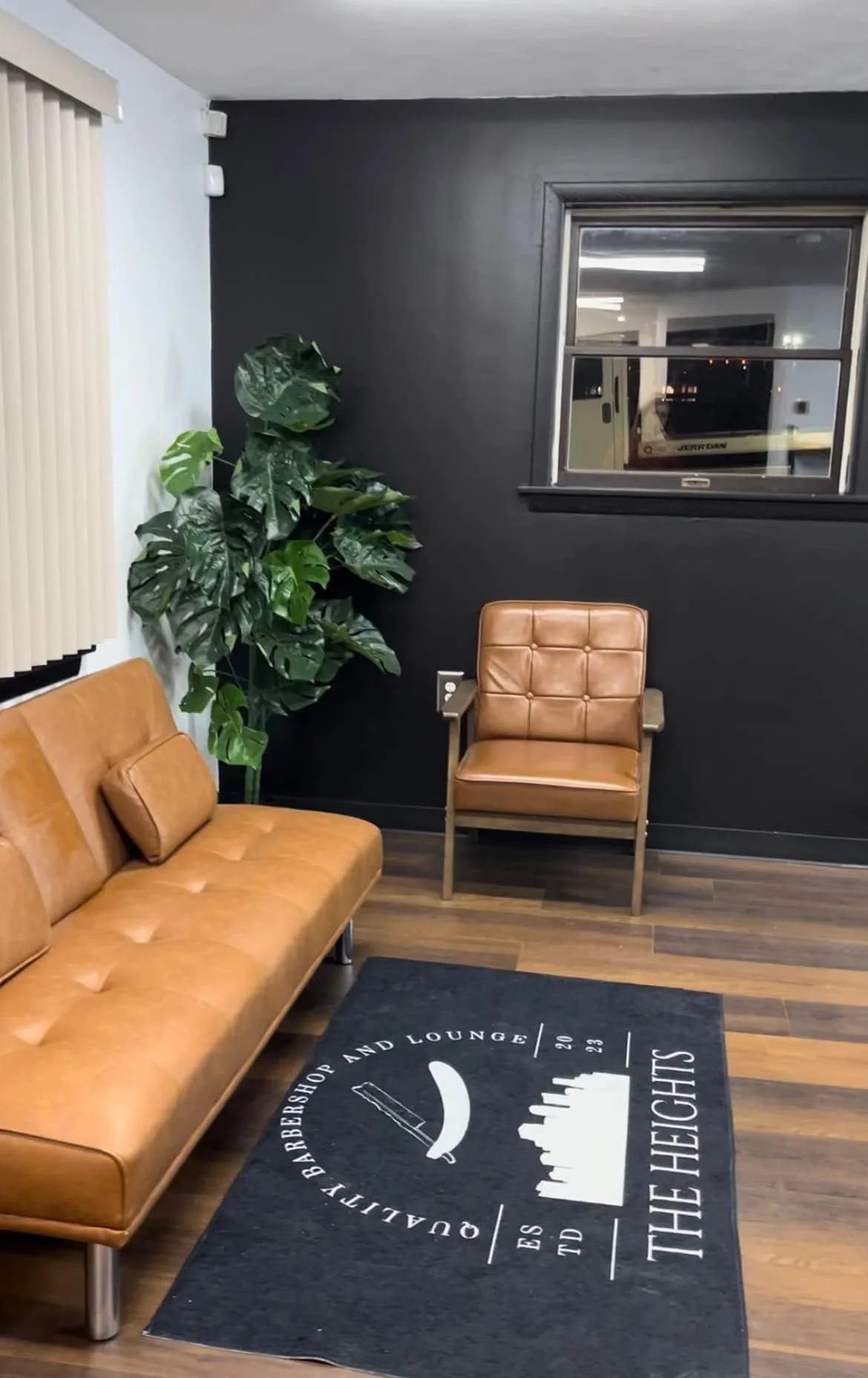 Interior of a modern lounge with brown leather sofa and chair, a green potted plant, a window with blinds, and a rug with a skyline logo and text.
