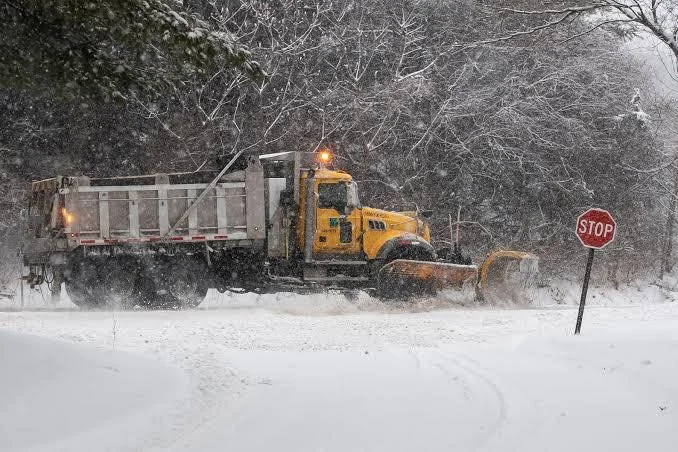 Yellow snowplow clearing snow near a stop sign during winter.