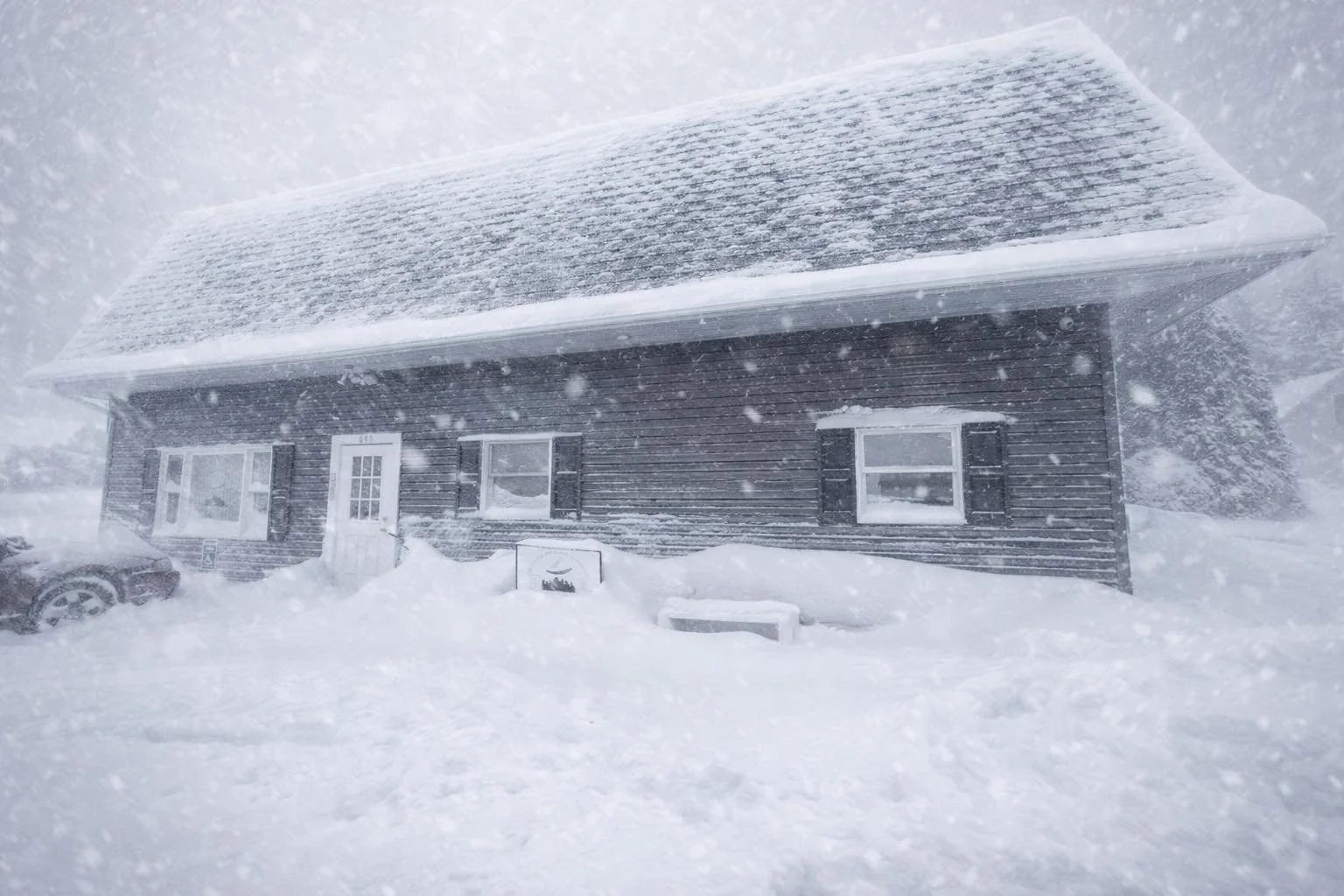 A snowy house with a pitched roof covered in snow, during a blizzard.
