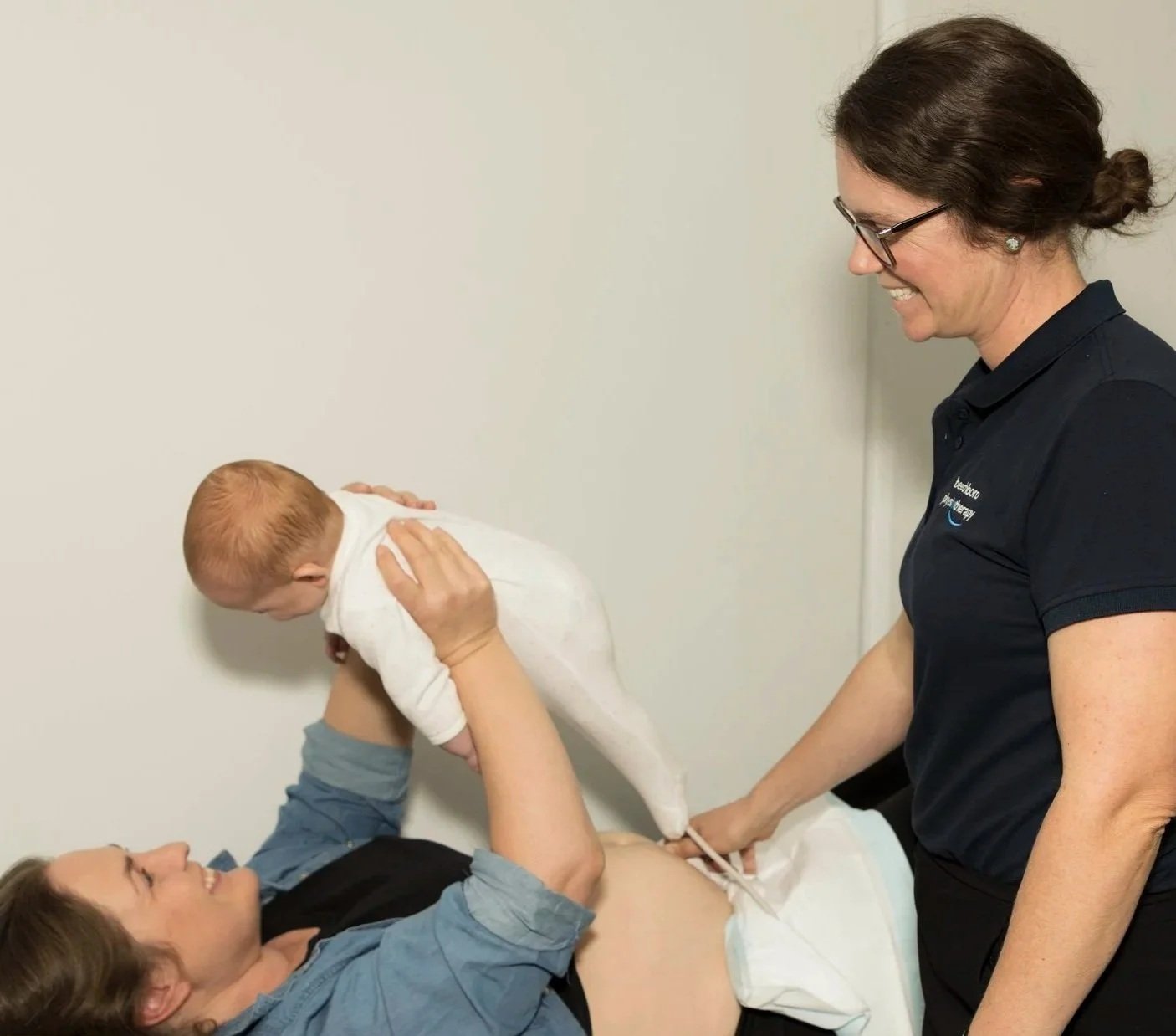 A woman giving birth in a medical facility while a healthcare professional assists and a baby is being placed on the woman's stomach.