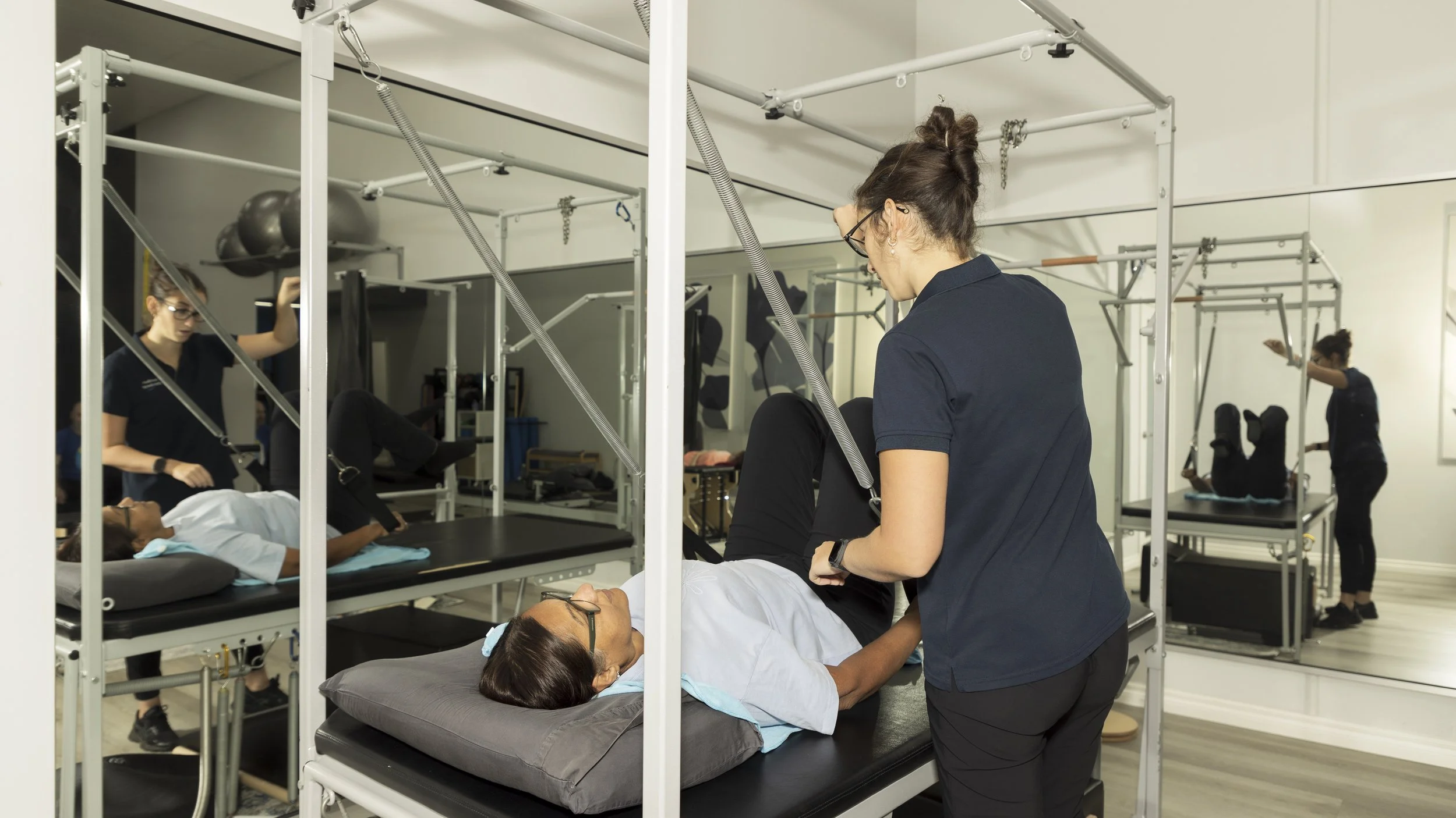 A physical therapy session where a therapist aids a patient with an exercise on a specialized table, with other patients and therapists in the background.