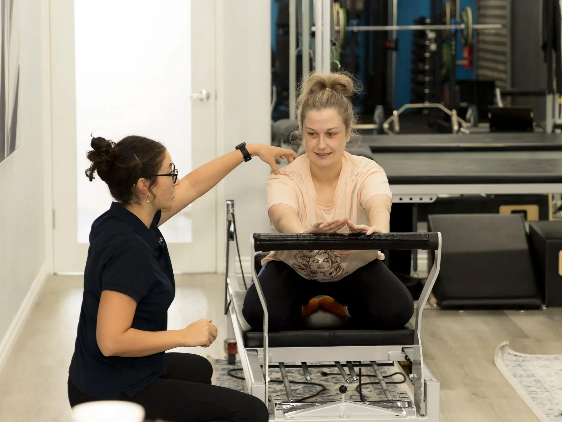 A therapist assisting a woman with a physical therapy exercise on a specialized table in a gym or rehabilitation center.