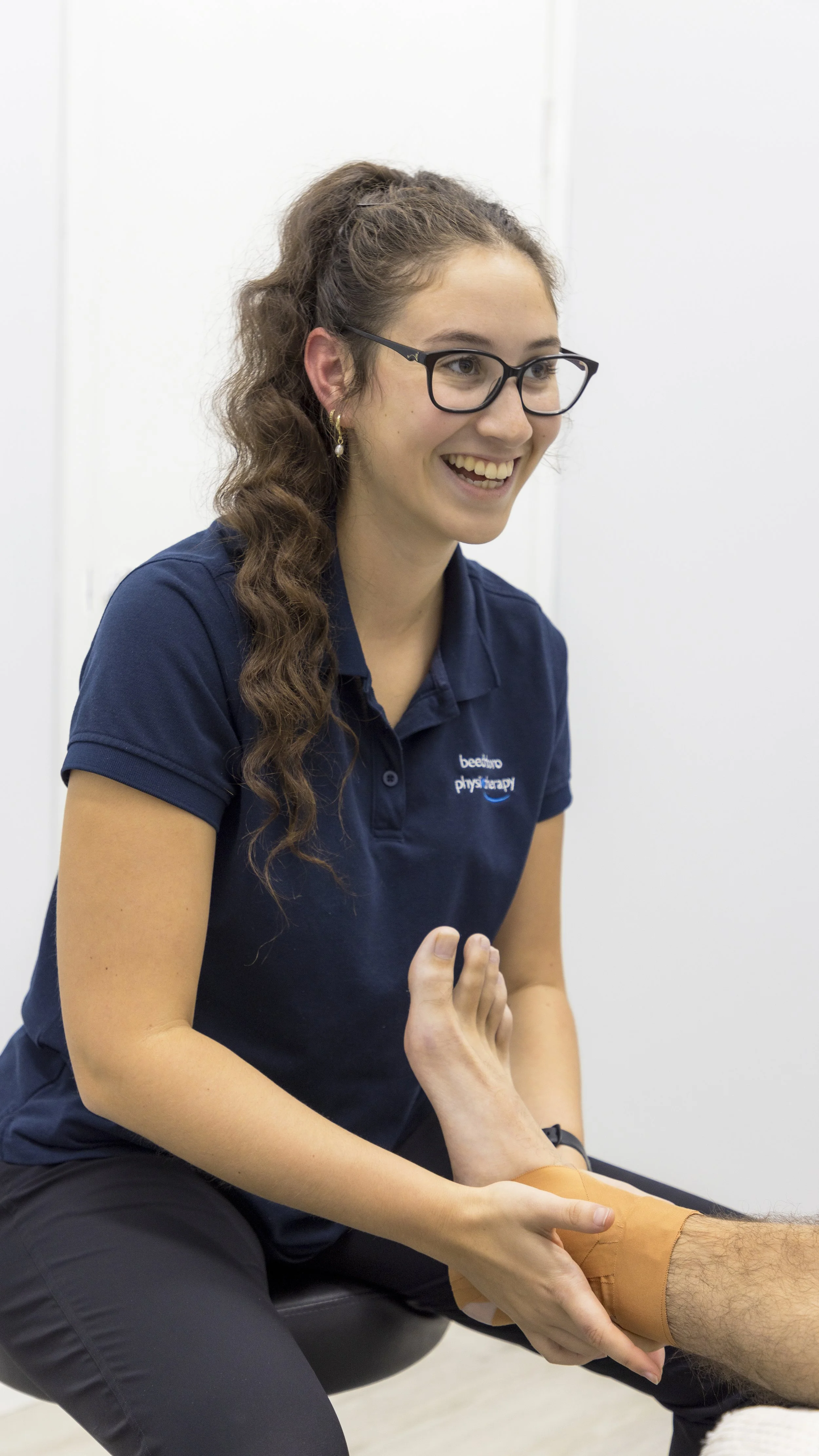 A physical therapist smiling while applying a strap around a patient's ankle during a therapy session.
