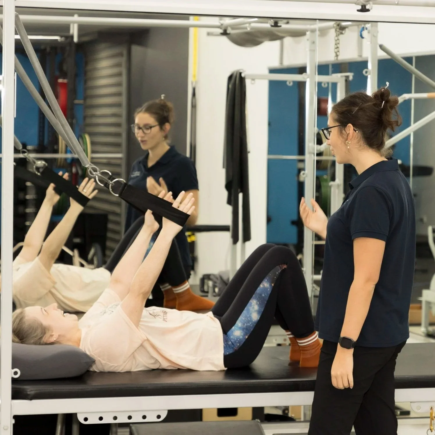 Girl lying on a therapy table pushing a resistance band upwards while two therapists assist her and a third therapist explains beside her.