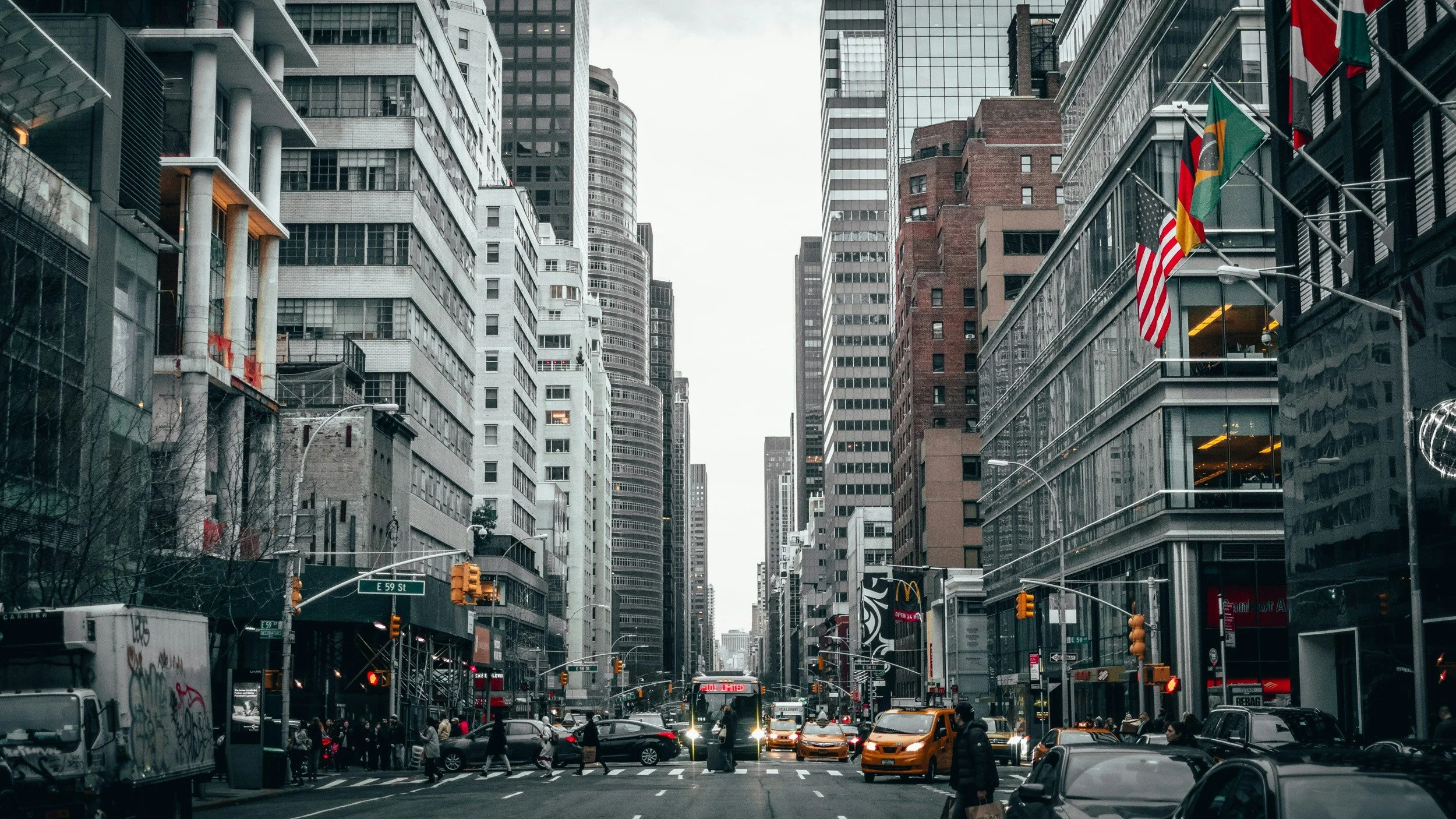 City street scene with tall buildings, traffic, pedestrians, and flags hanging from buildings.