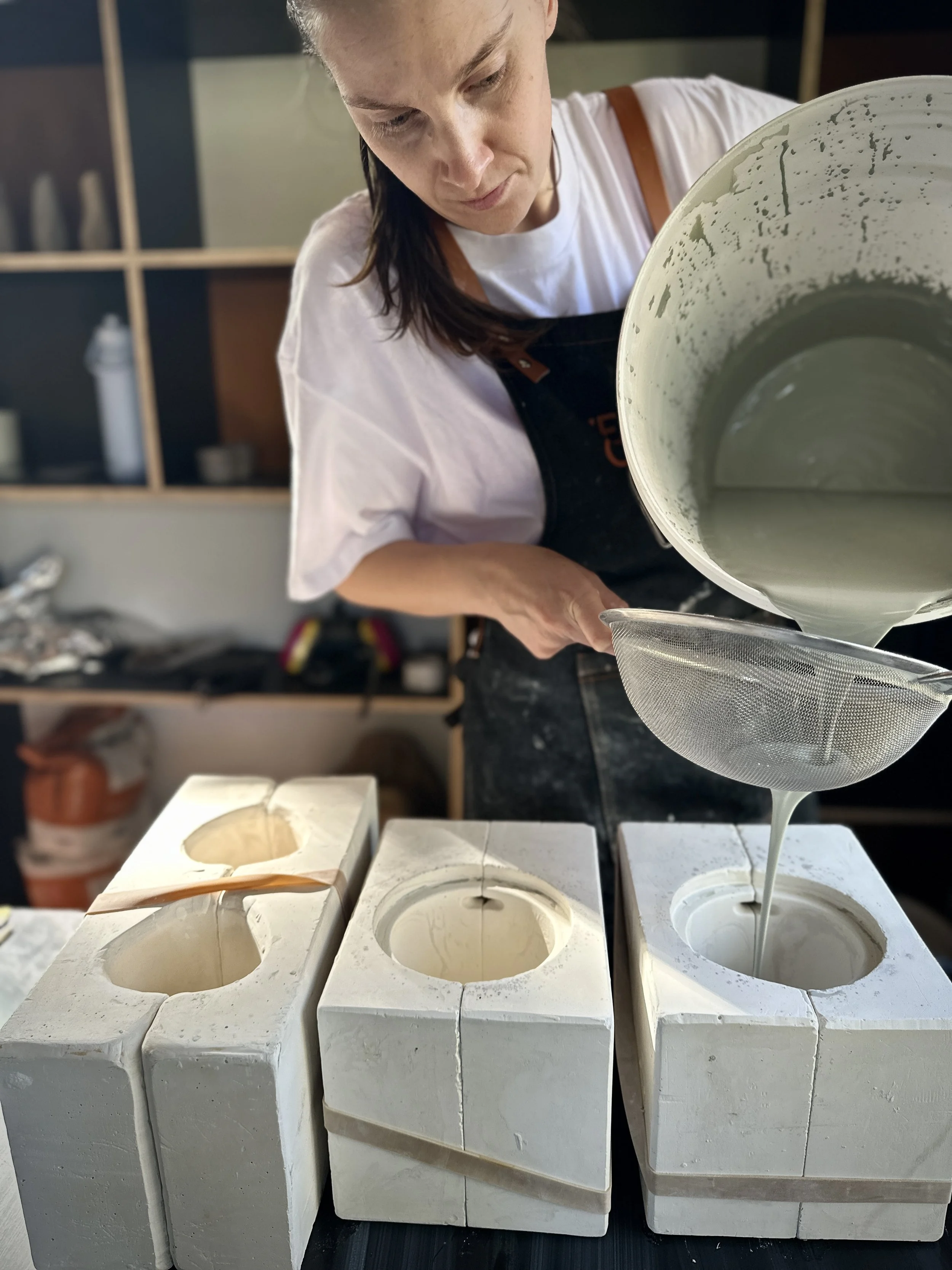 Woman pouring Moss (Green) coloured porcelain slip in to mug mould in her Adelaide ceramics studio