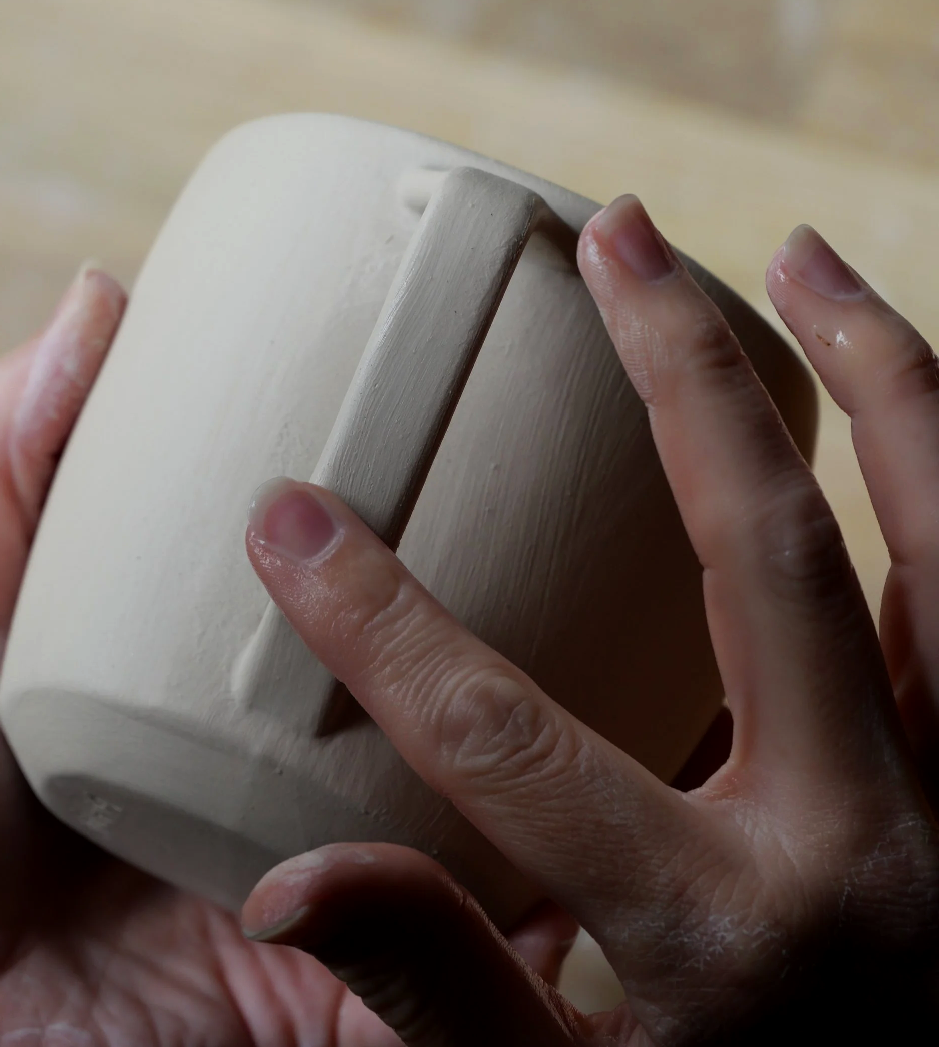 person smoothing a ceramic cup handle slip cast part line