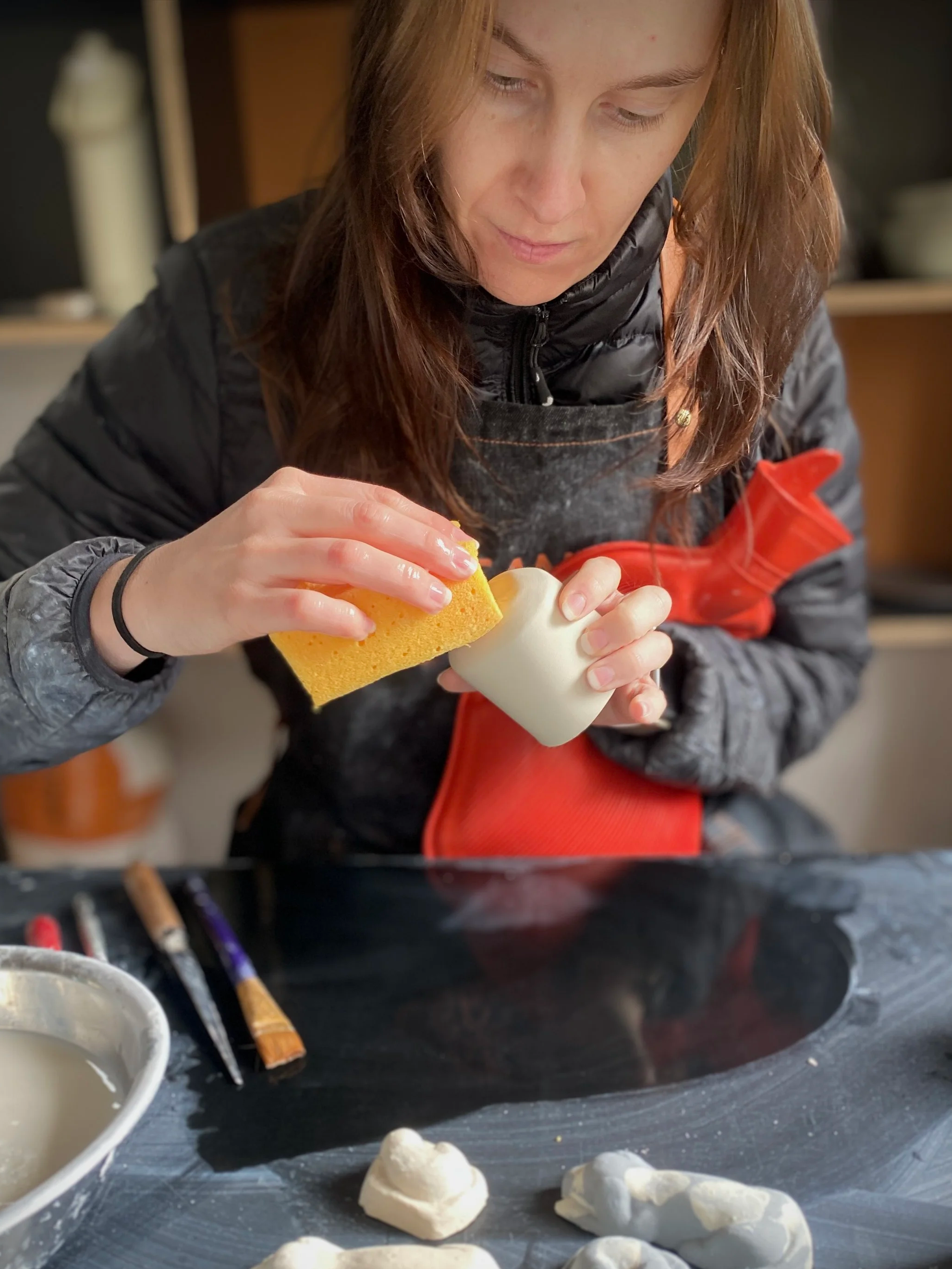 Woman working in a cold ceramic studio with a puffer jacket and hot water bottle