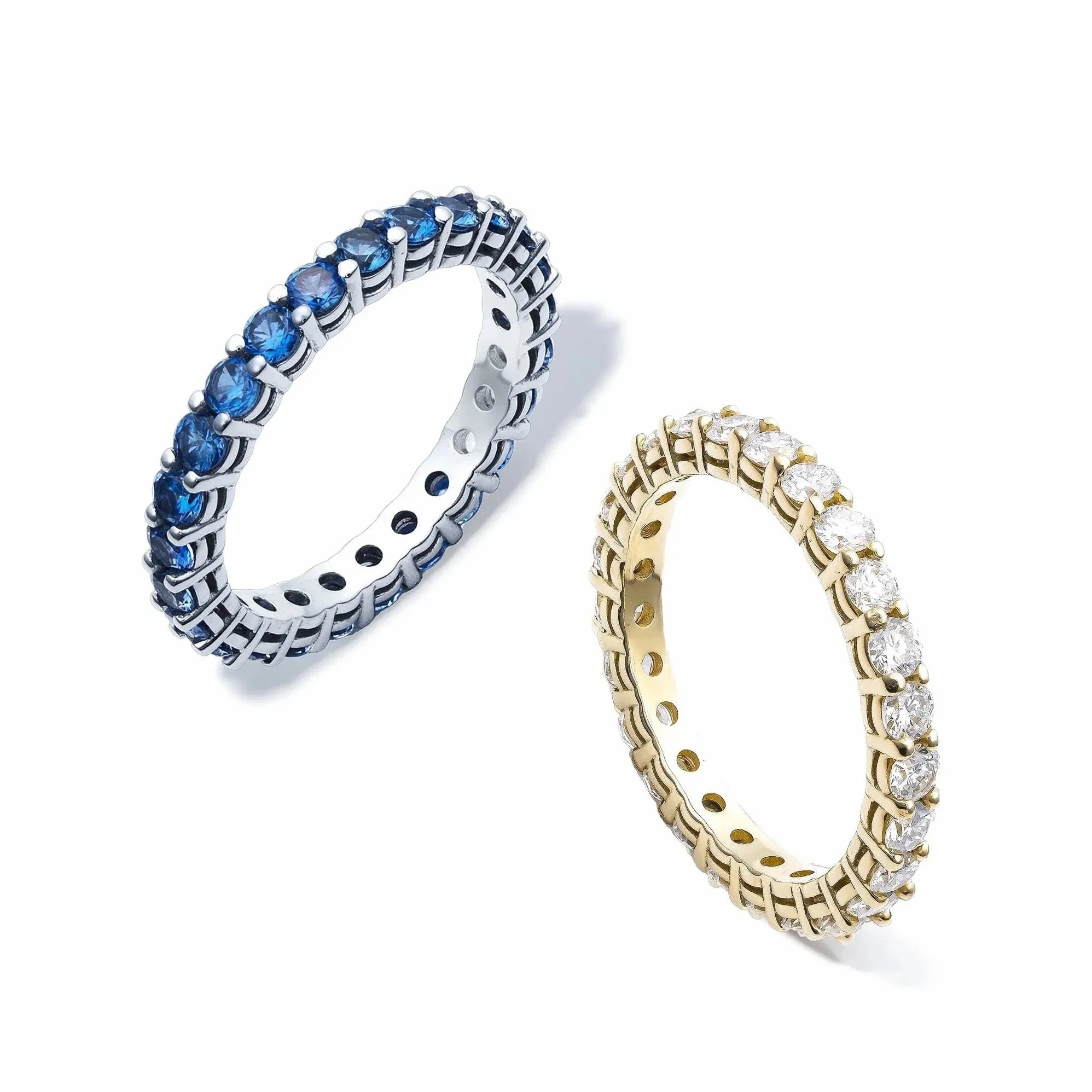 Close-up of three rings with gemstones: one wide silver band with blue gemstones, one narrower gold band with clear gemstones, and a third gold band with clear gemstones.