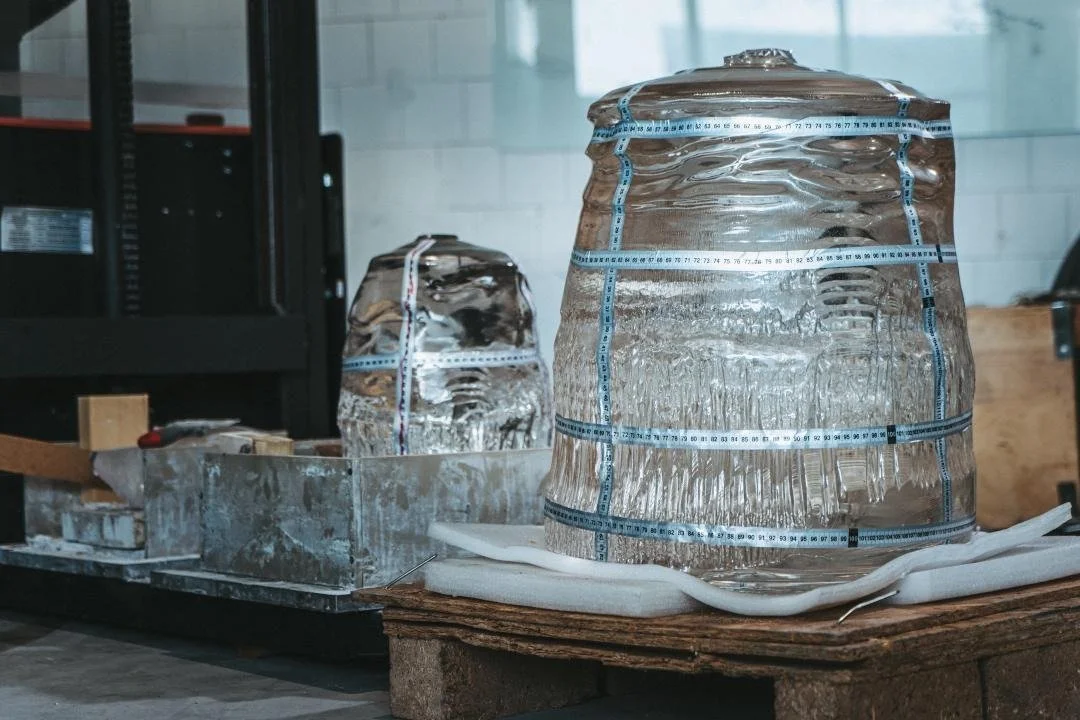 Two glass containers filled with ice, with measuring tapes wrapped around them, on a wooden surface in a workshop setting.