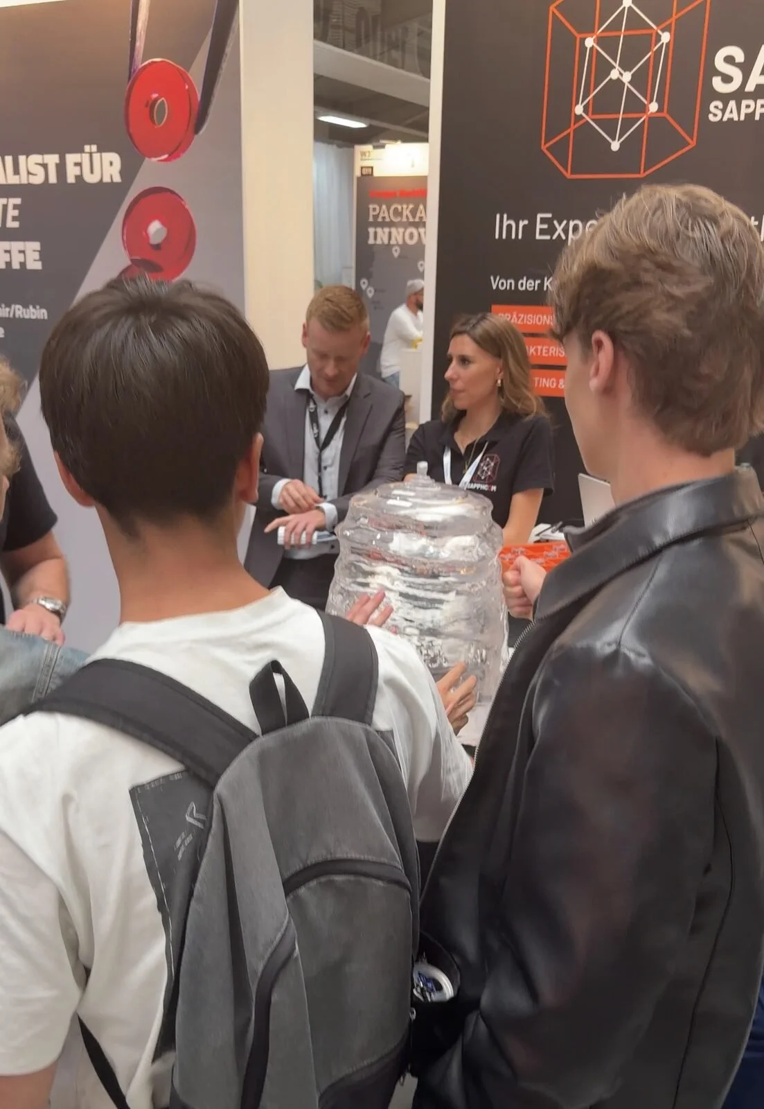 Visitors gather around the 100 kg sapphire boule during a live demonstration at the SAPPHCOM booth and touch the crystal