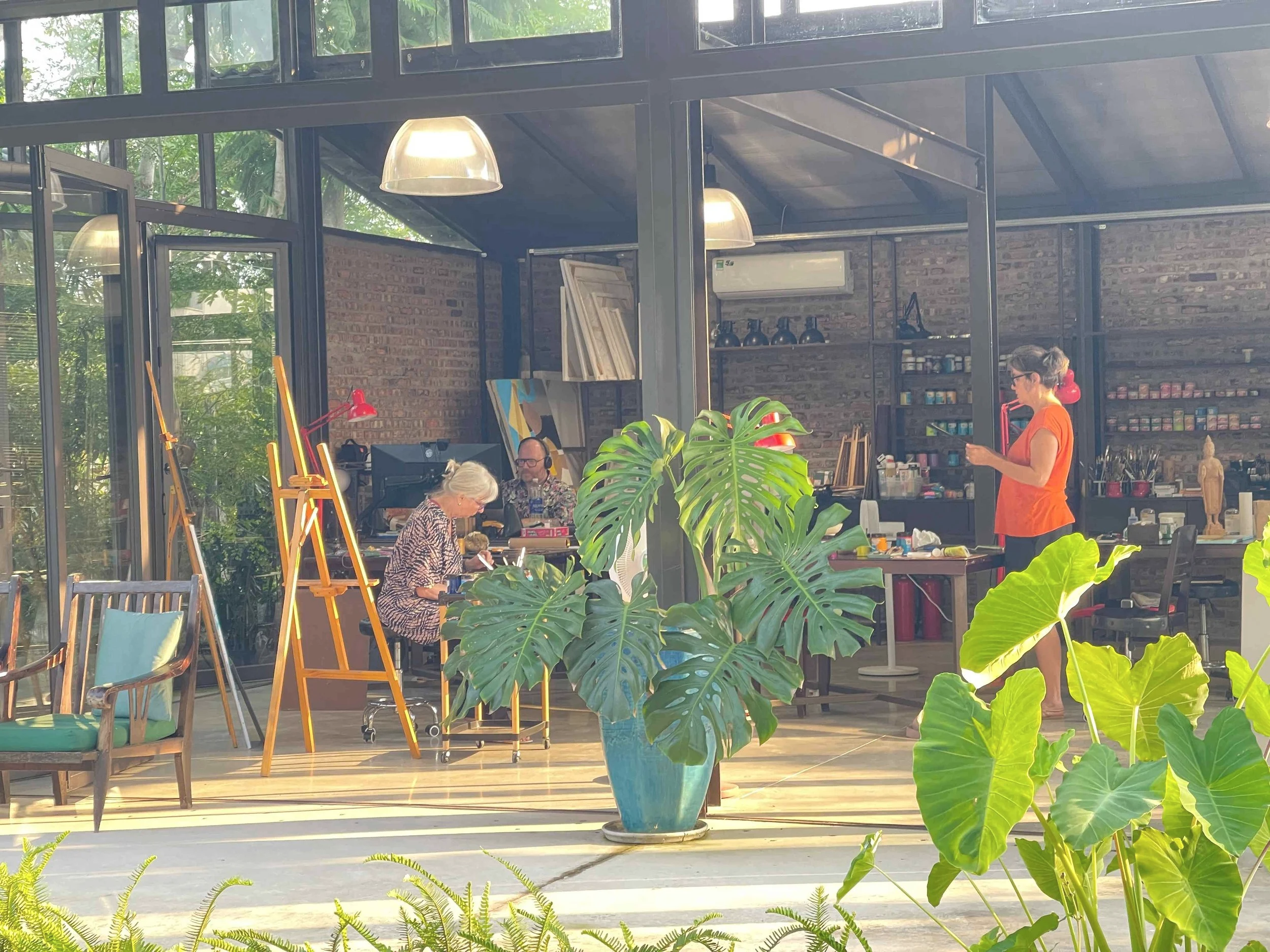 guests in art studio and on terrace working on their own art projects with lush greenery in front