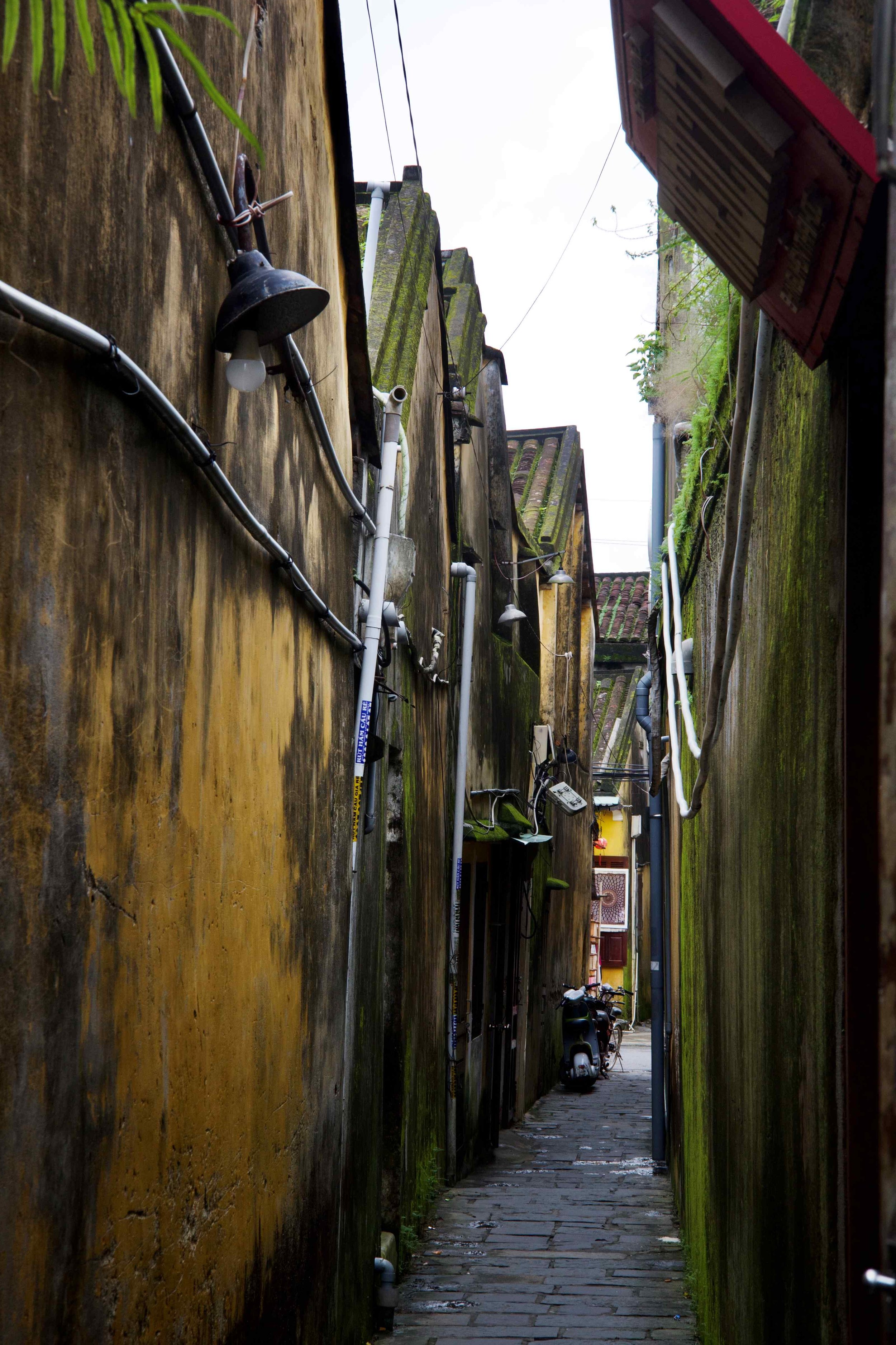 small alley way of Hoi An Old Town showing withered yellow walls