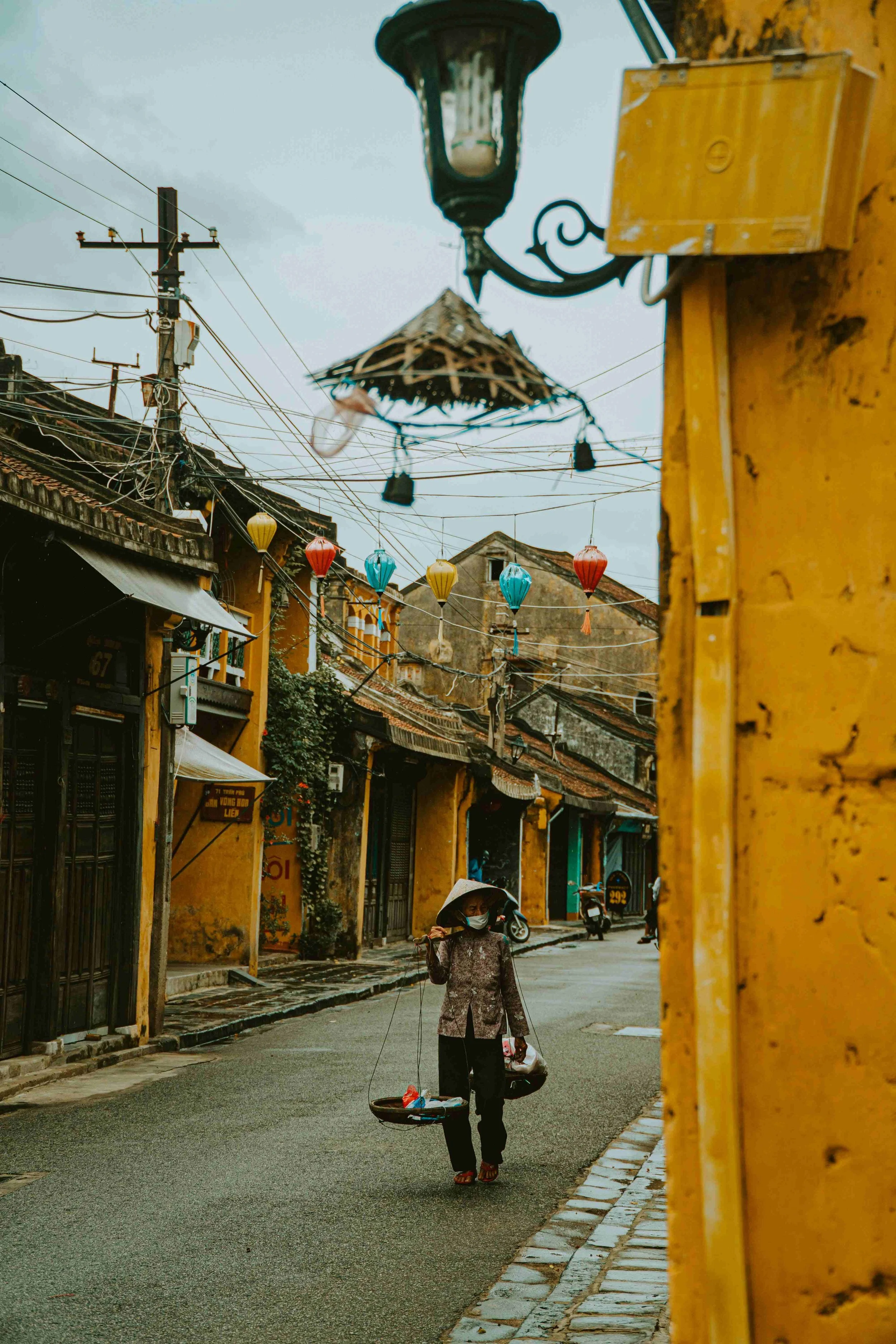 Vietnamese woman walking through Hoi An old town carrying two baskets and a Vietnamese hat