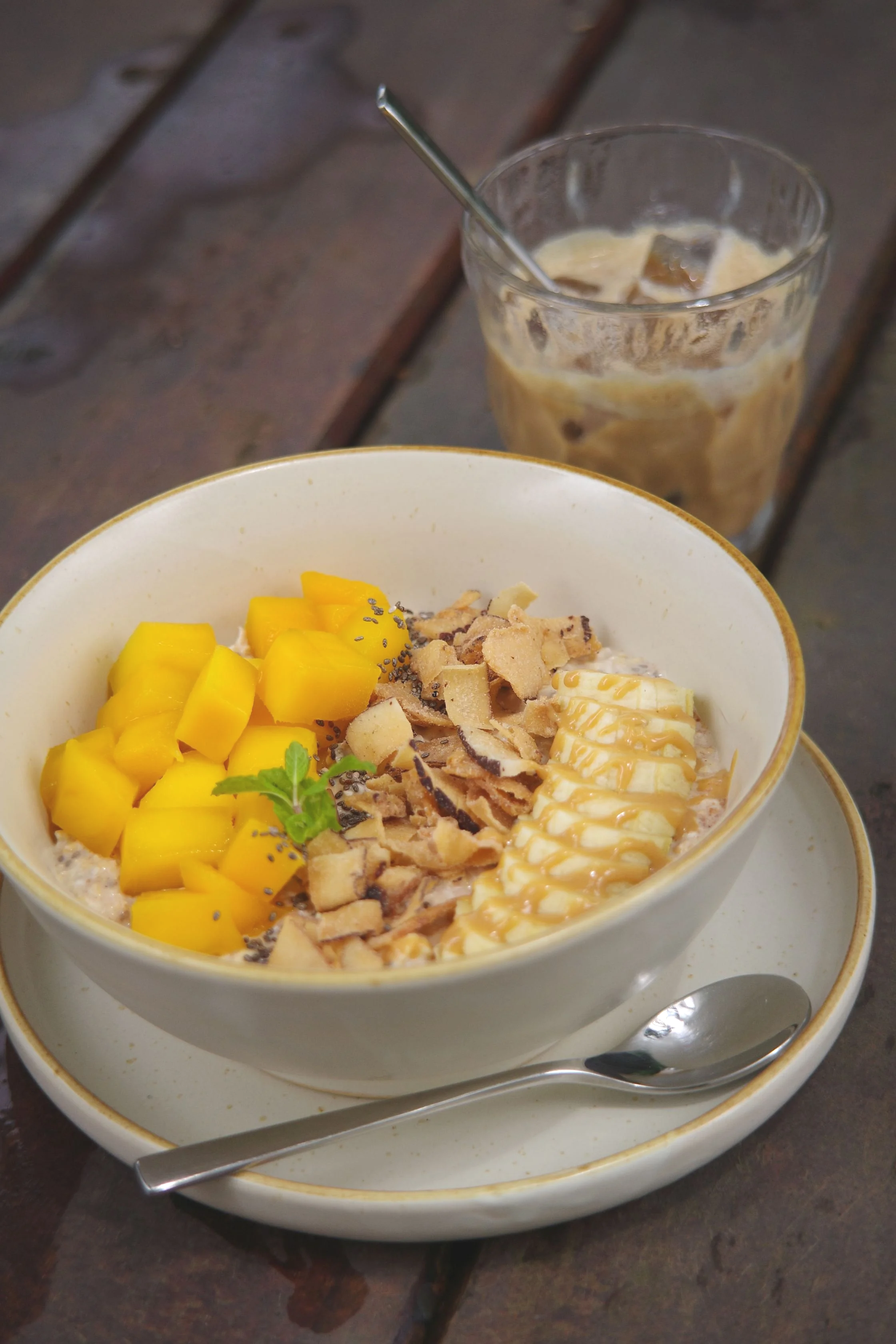 breakfast bowl with overnight oats mango banana and iced coffee